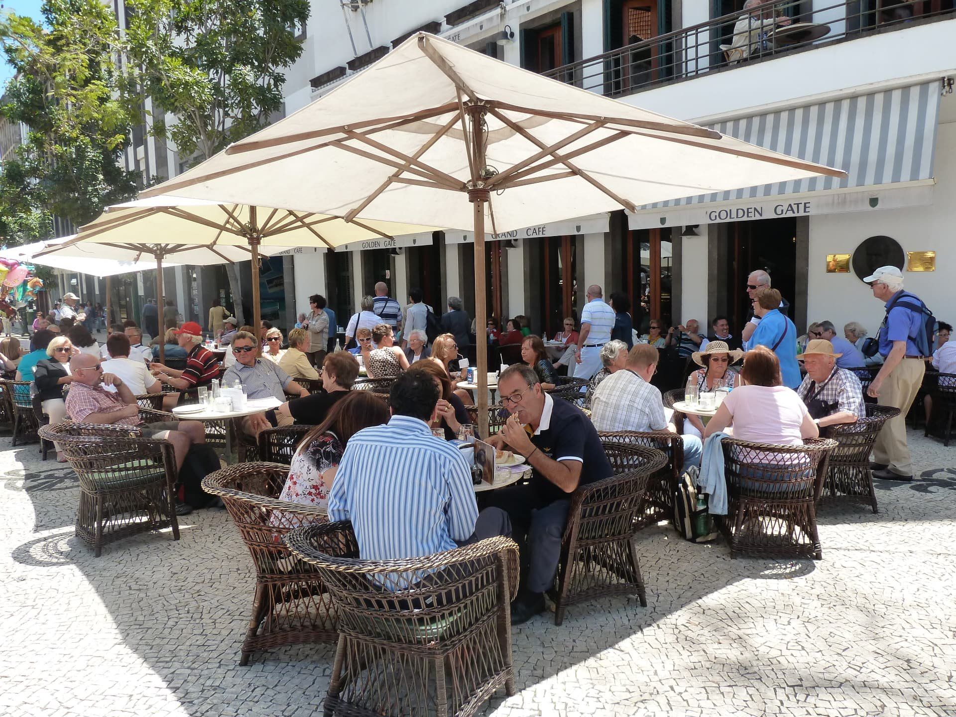Busy outdoor café terrace in Funchal with umbrellas and Portuguese calçada paving.
