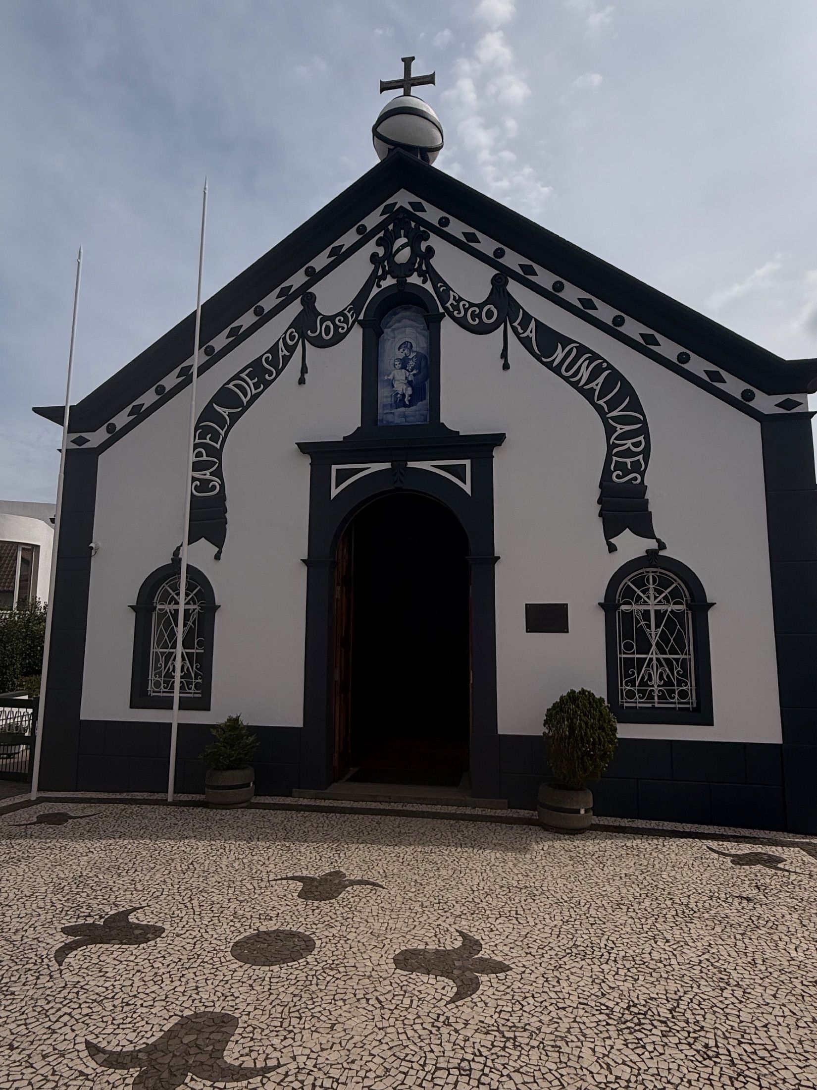 Capela de Sao Jose - Fachada branca de capela com remates escuros, porta em arco aberta e calçada com padrões