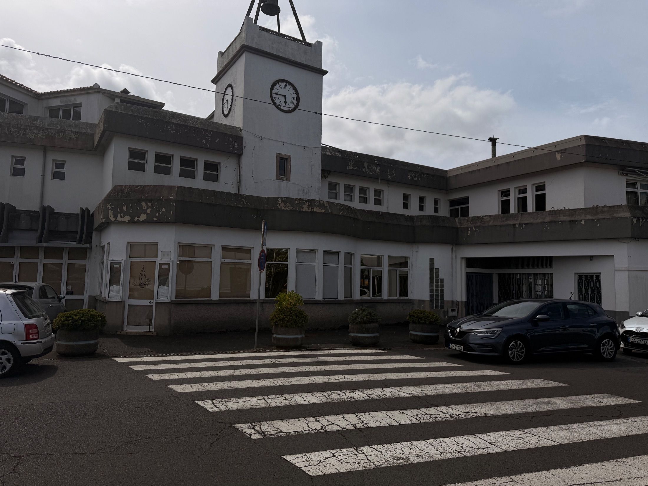 Café Relógio Edifício branco com torre de relógio e sino, atrás de uma passadeira e carros estacionados