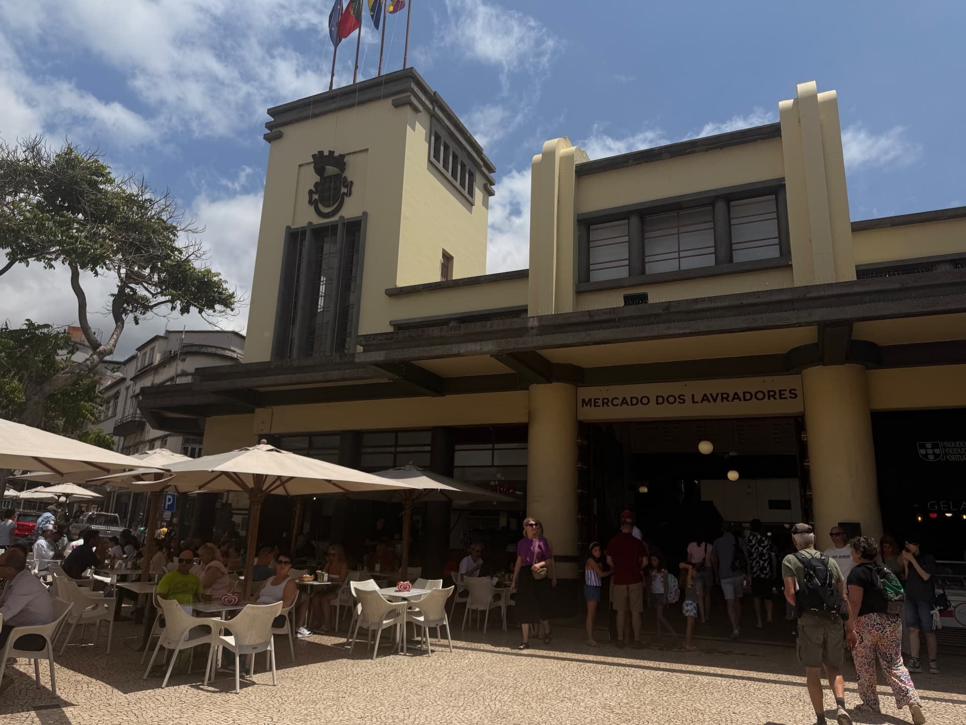 Mercado dos Lavradores exterior with flags on the tower, cafe terraces and shoppers, Funchal.