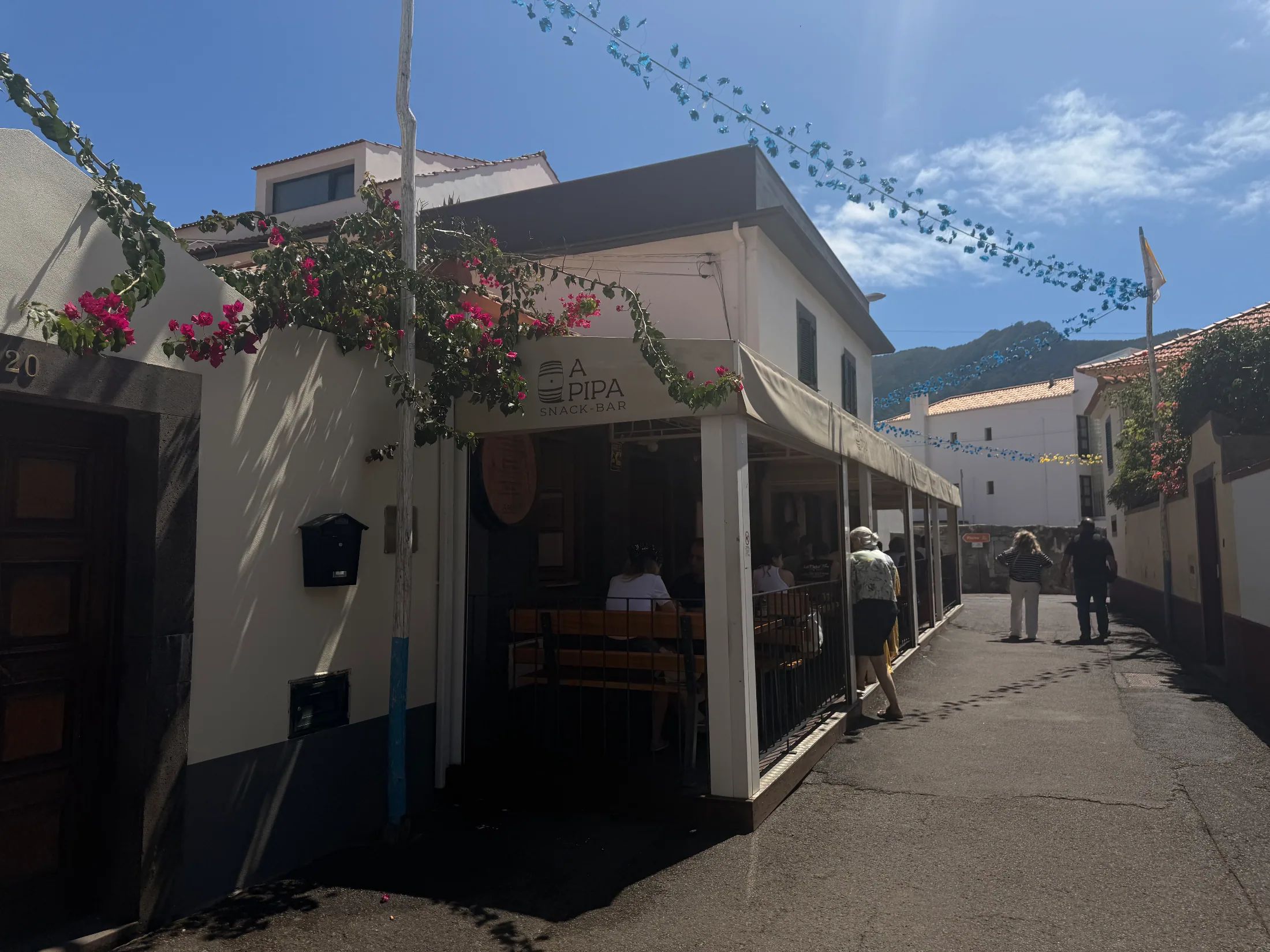 A Pipa Snack-Bar terrace on a narrow street with blue bunting and pink bougainvillea flowers.