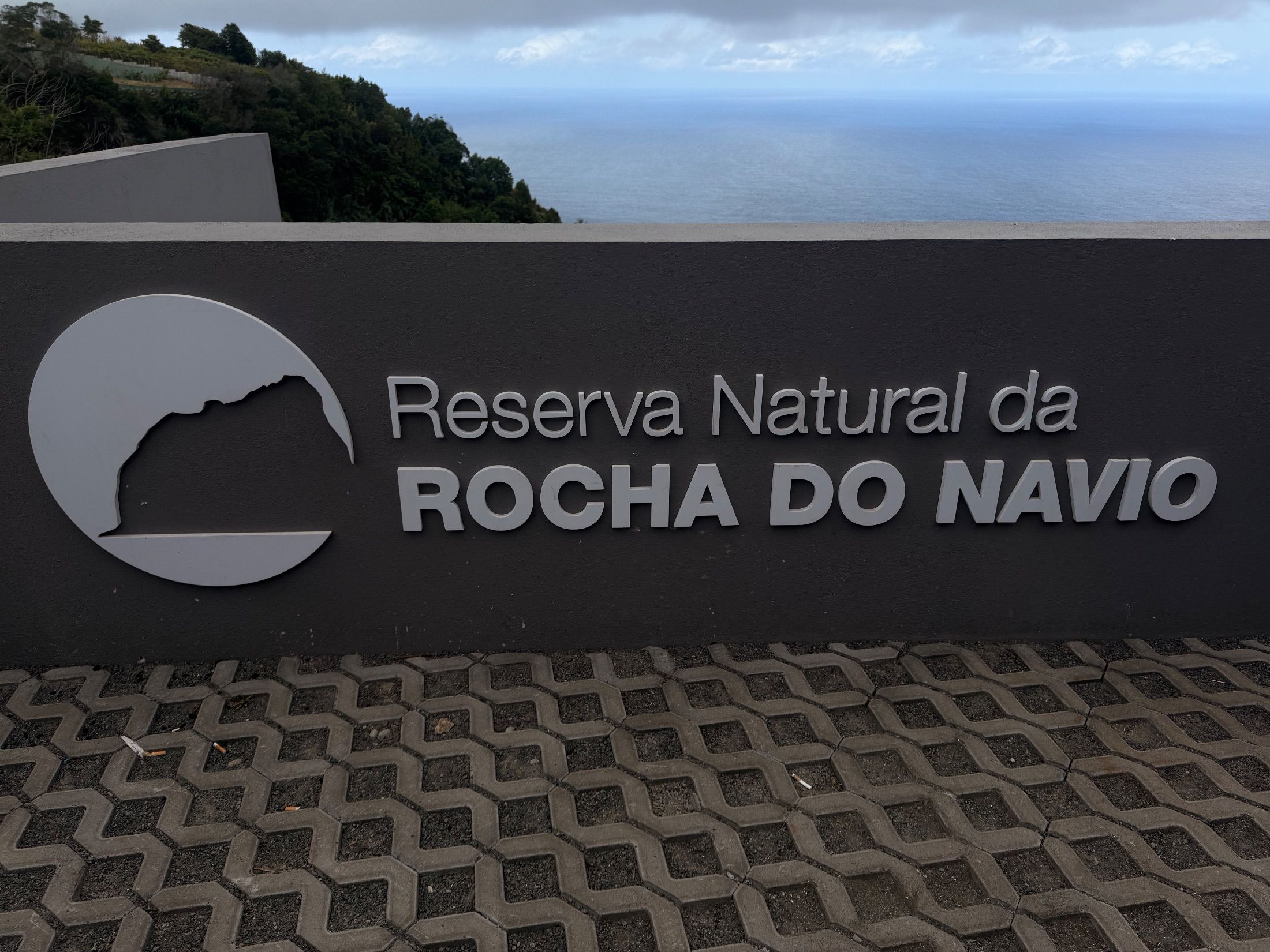 Rocha do Navio Nature Reserve sign with sea and wooded hillside behind