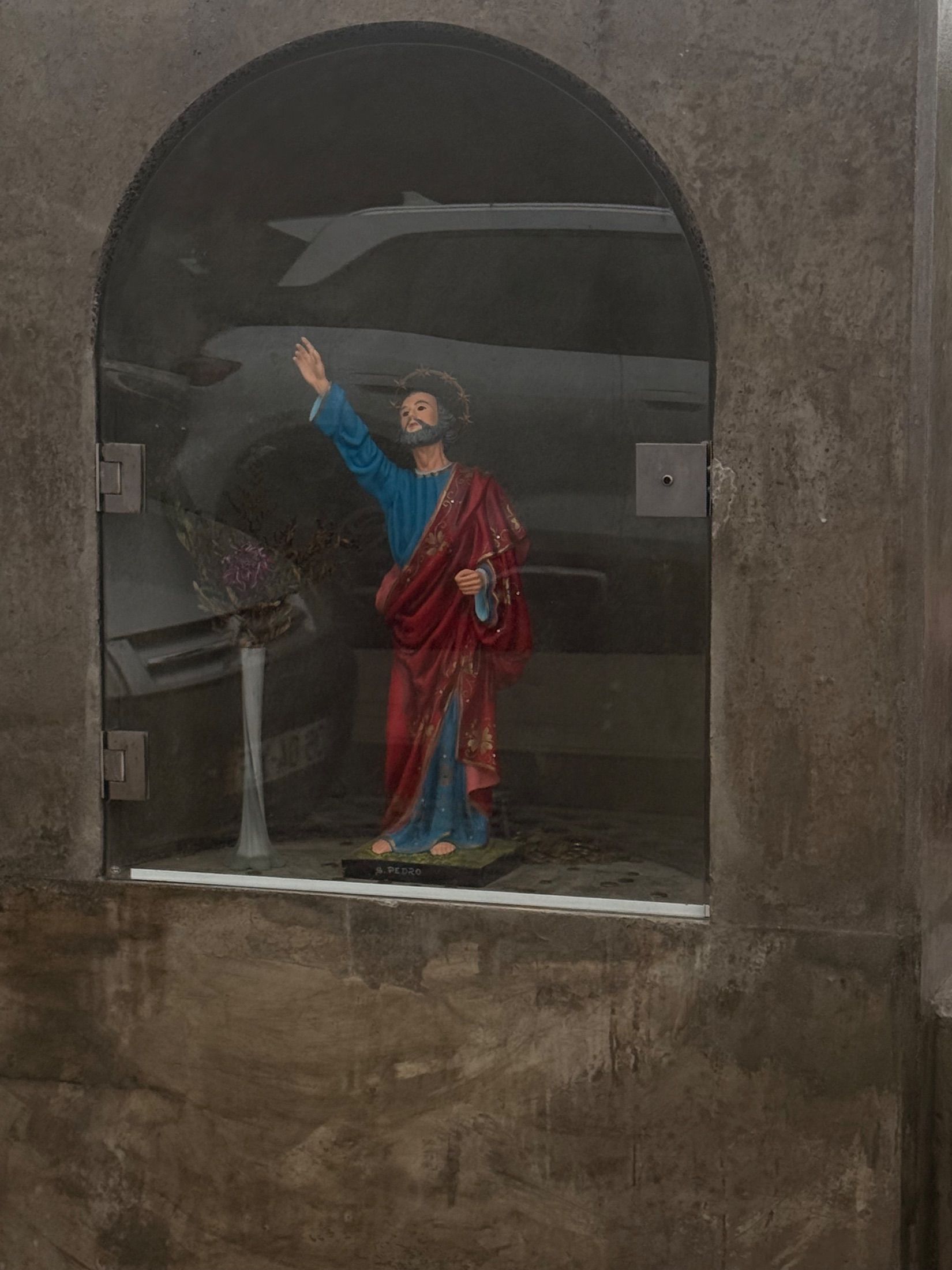 Statue of Saint Peter in red and blue robes behind glass in an arched niche