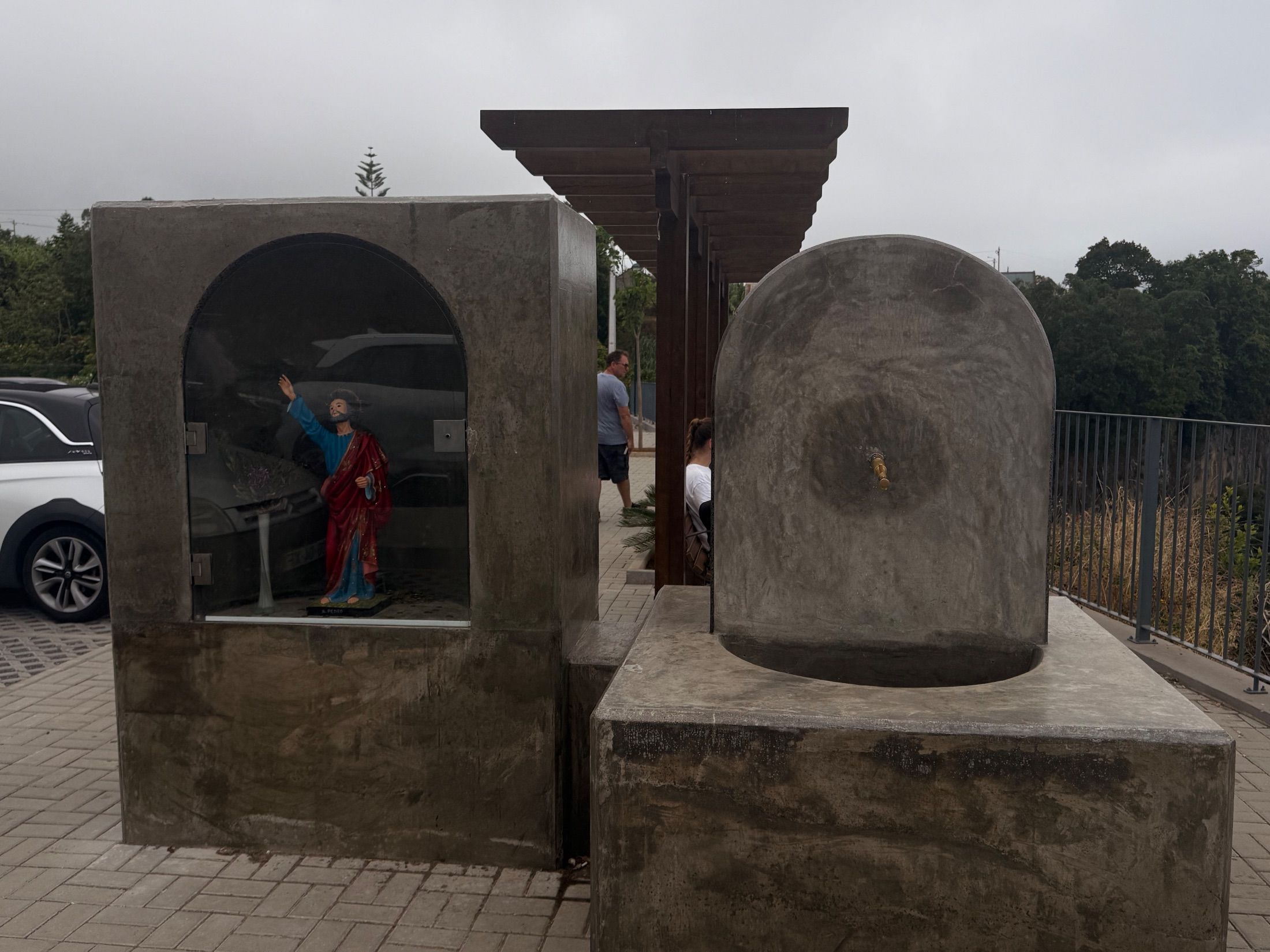 Concrete fountain beside a glass-fronted shrine containing a painted religious statue