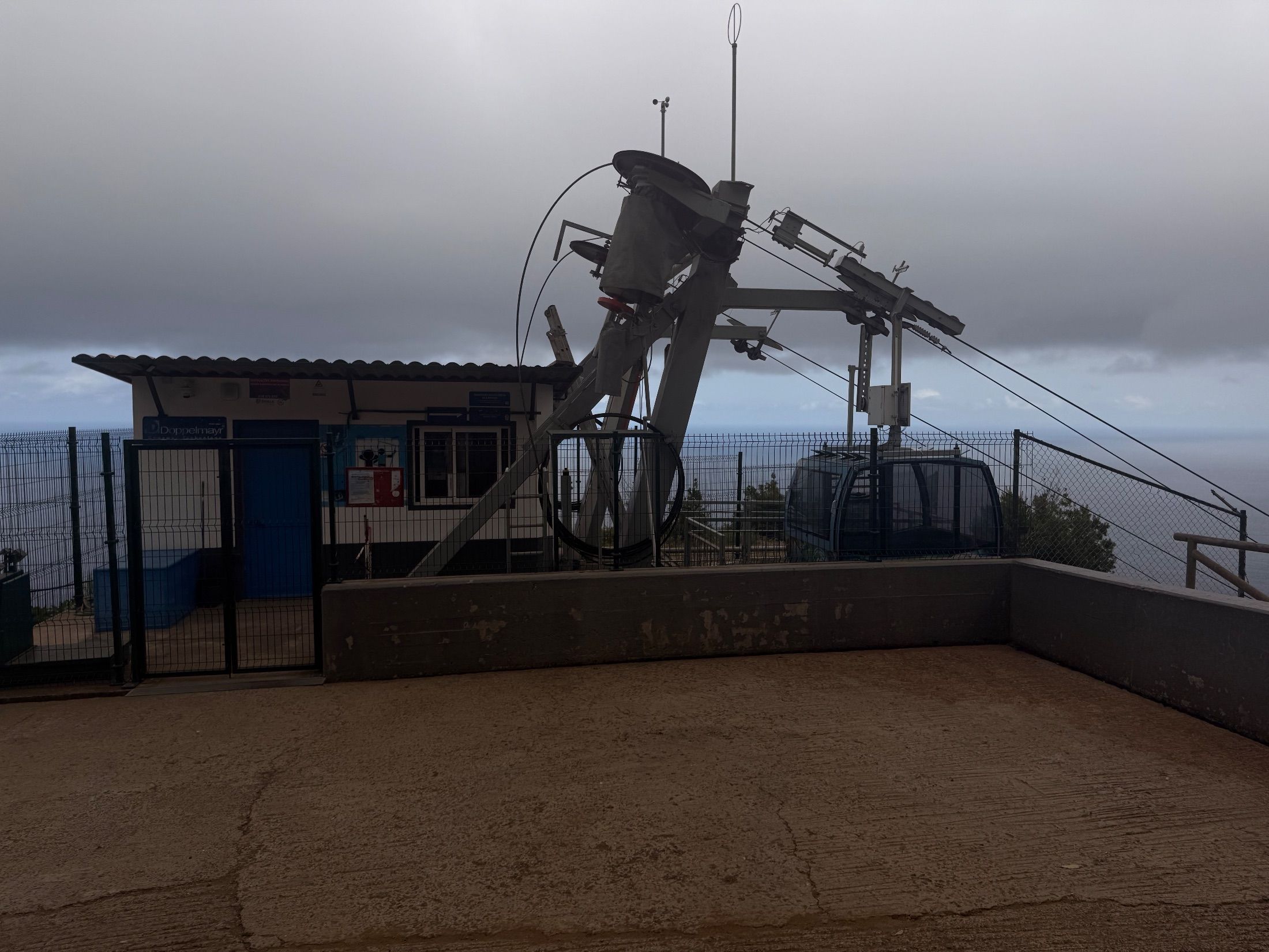 Cable car cabin and fenced station overlooking the sea beneath grey clouds