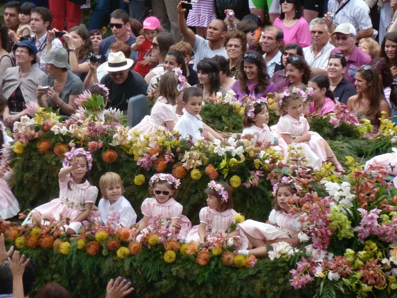 Children in flower crowns riding a flower-covered float in the Madeira Flower Festival parade.