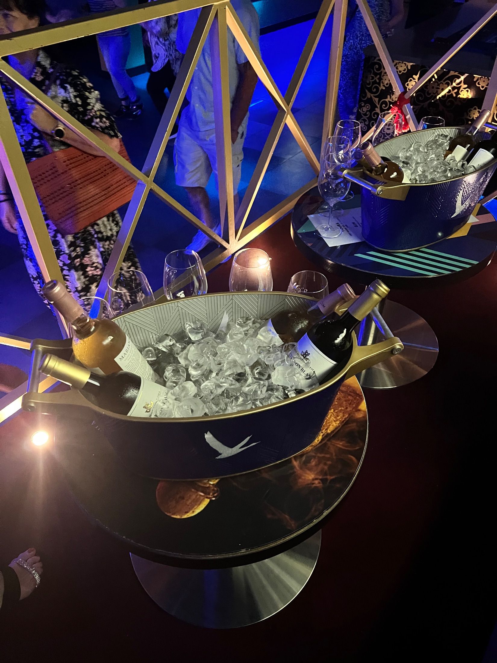 Wine bottles in ice buckets on nightclub tables beside a gold-coloured railing