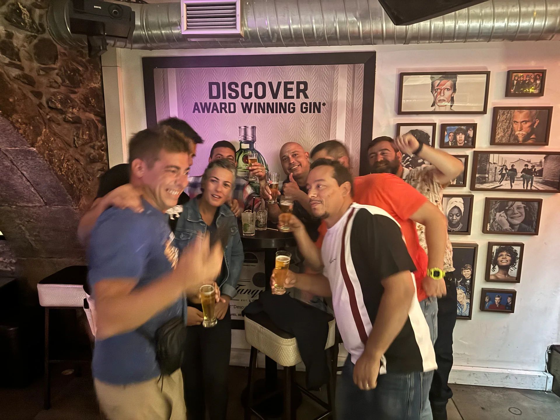A group raising drinks inside Lust Vintage in Funchal, beside a wall of framed music-legend photos
