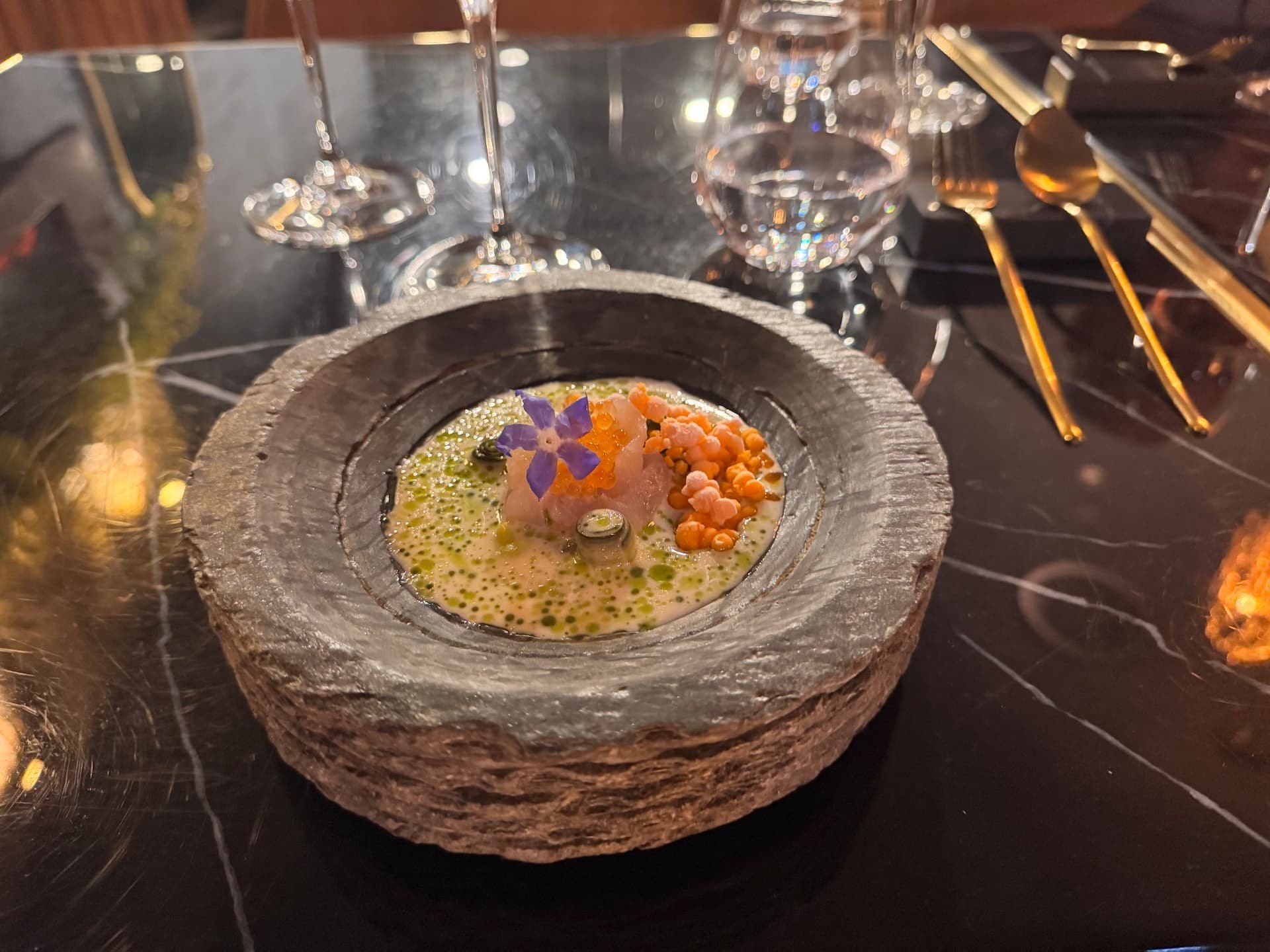 Tártaro de peixe curado com ovas e flores comestíveis numa taça esculpida em pedra vulcânica no Audax Funchal