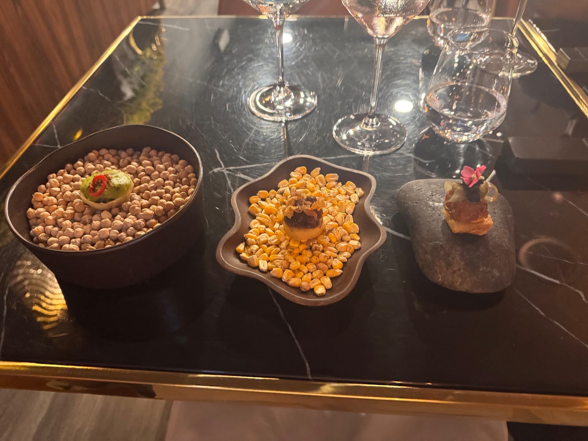 Trio de petiscos do menu de degustação do Audax Funchal, servidos sobre grão-de-bico, grãos de milho e pedra vulcânica