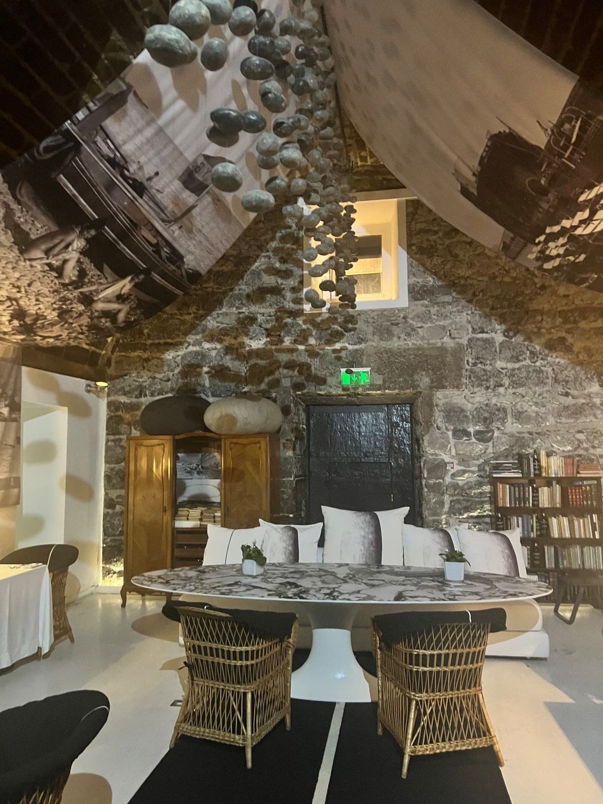 Interior dining room at Design Centre Nini Andrade Silva in Funchal, with exposed stone walls, wicker chairs and suspended pebble artwork