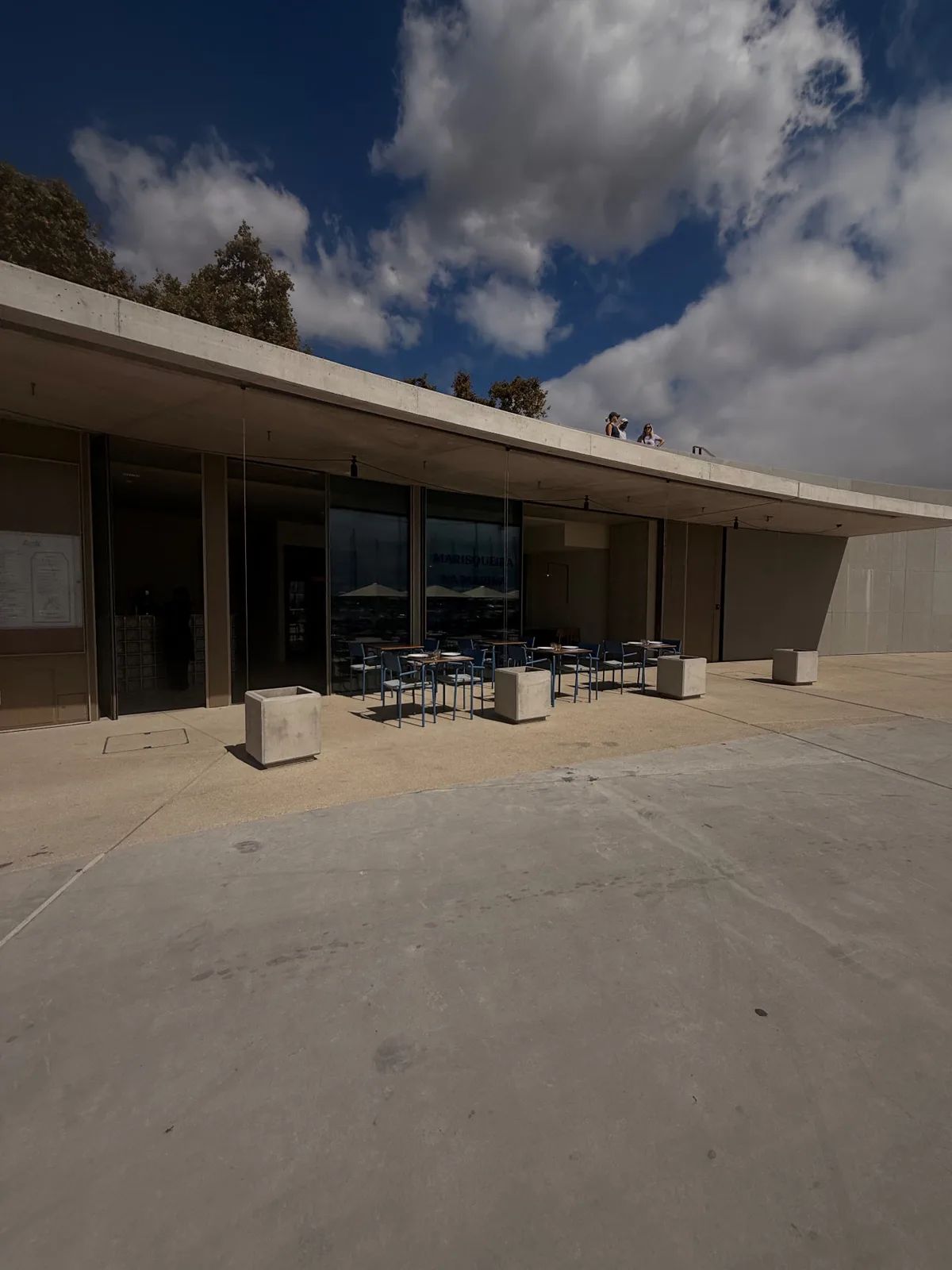 Glass frontage of Marisqueira na Marina with blue chairs under a concrete canopy