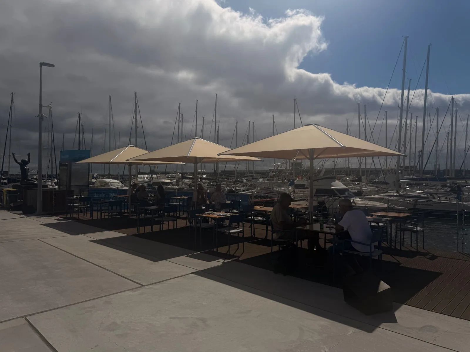 Diners under cream parasols on the Marisqueira na Marina deck, yachts behind
