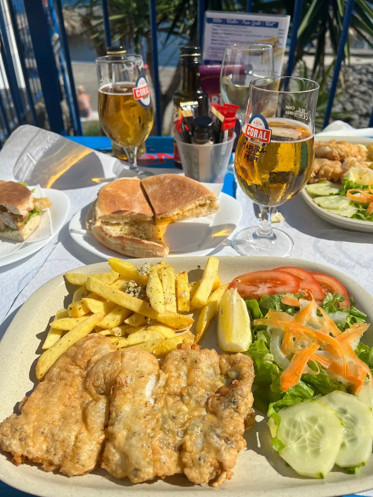 Plate of fried fish with chips, salad and a Coral beer on a sunny terrace table at Nova Onda