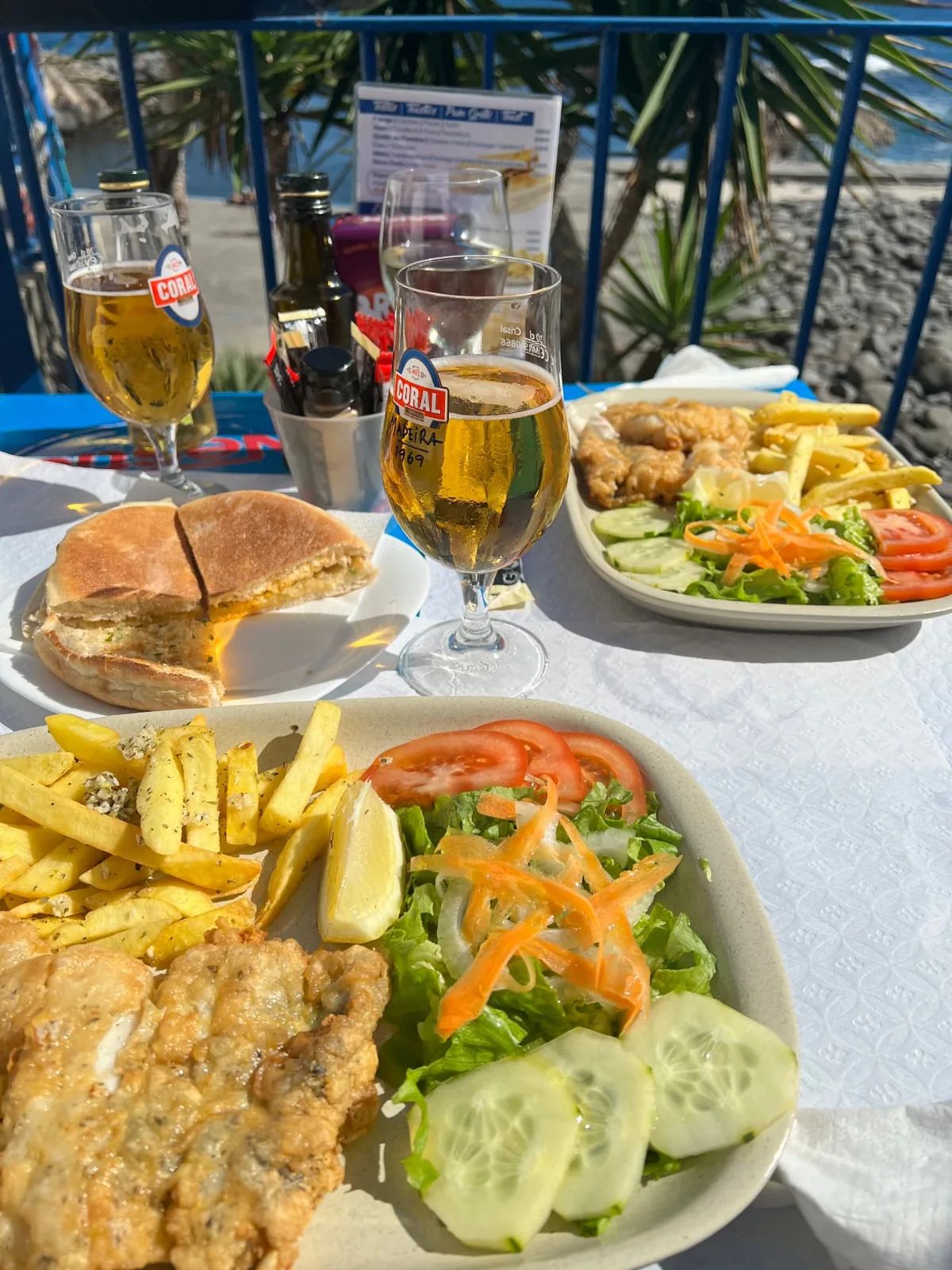 Almoço à base de peixe frito, sanduíche de prego e cervejas numa mesa de esplanada à beira-mar, junto à praia de seixos da Nova Onda