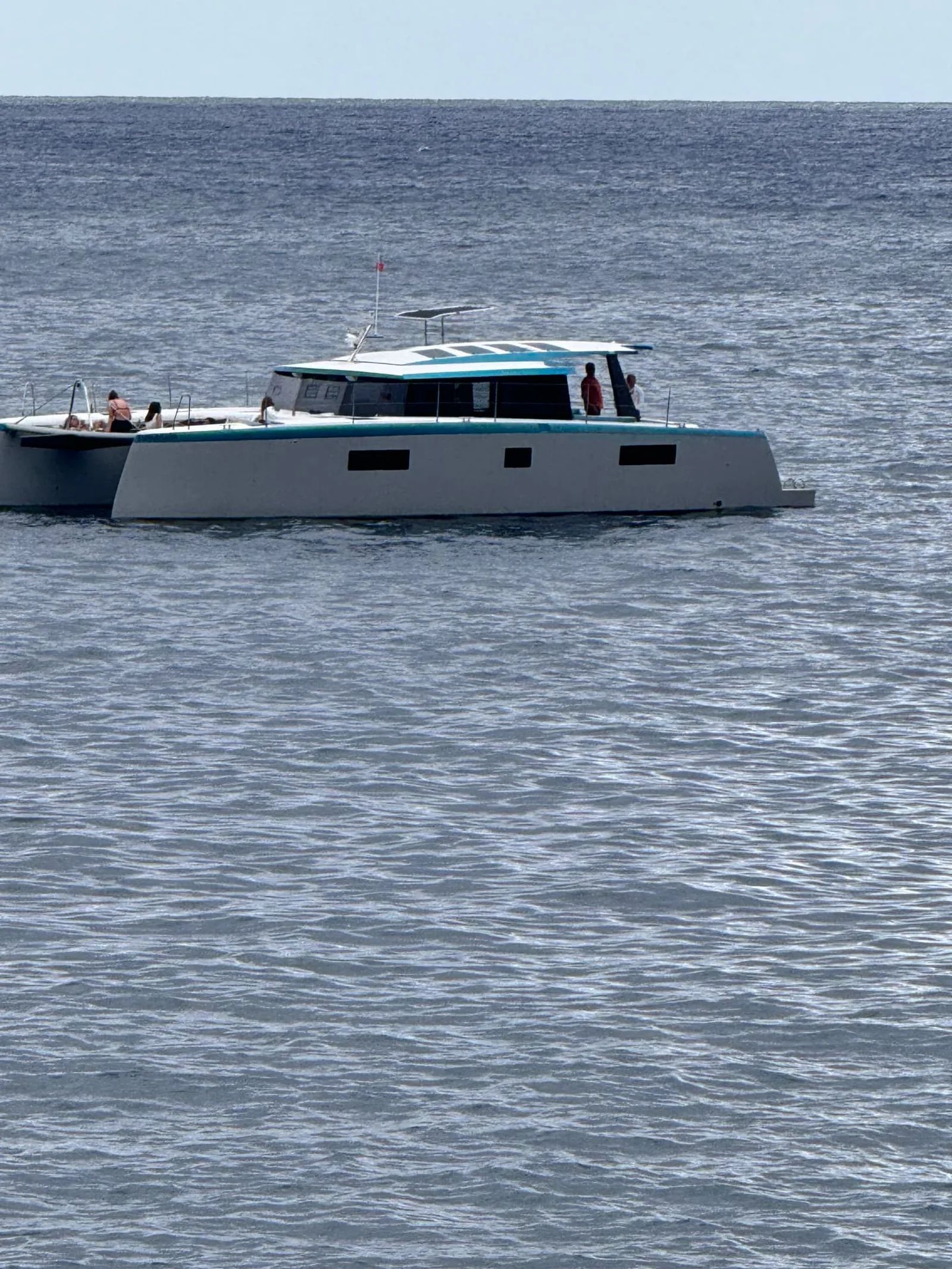 Catamaran passing offshore on calm blue water seen from the seafront at Garajau