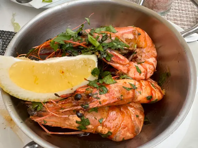Pan of large grilled prawns with coriander, lemon and pepper sauce on a table at Bar Restaurante O Mero in Garajau