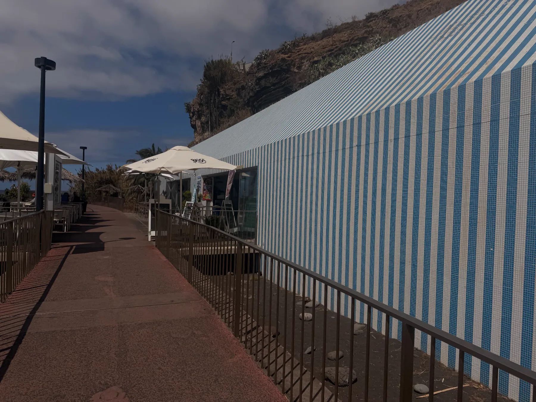 Blue-and-white tiled Restaurante Praia Formosa beside the seaside promenade in Funchal, with outdoor tables and a rocky hillside behind.