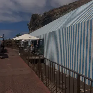 Blue-and-white tiled Restaurante Praia Formosa beside the seaside promenade in Funchal, with outdoor tables and a rocky hillside behind.