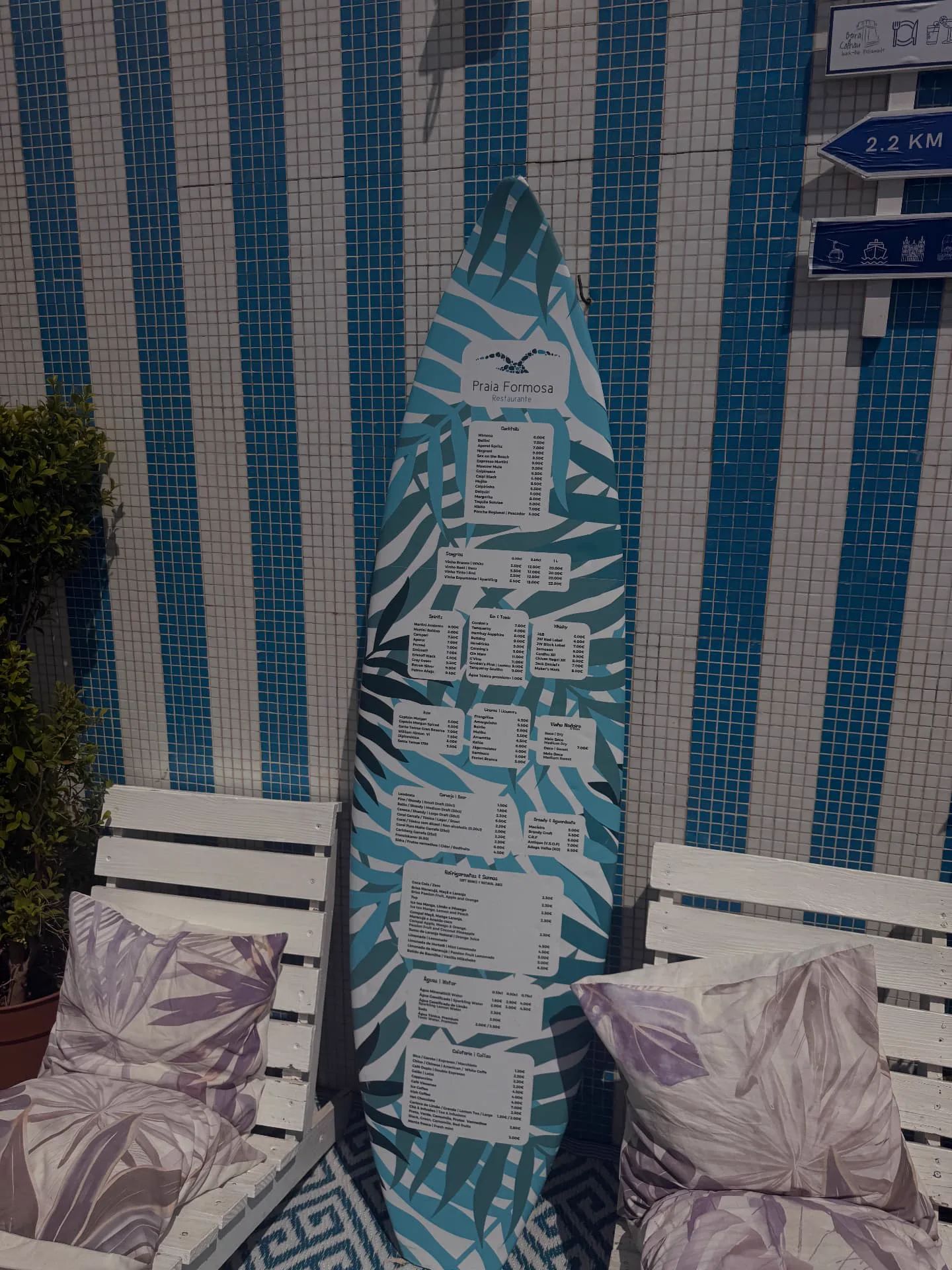 Surfboard-shaped menu beside cushioned terrace chairs at Restaurante Praia Formosa overlooking the Atlantic.