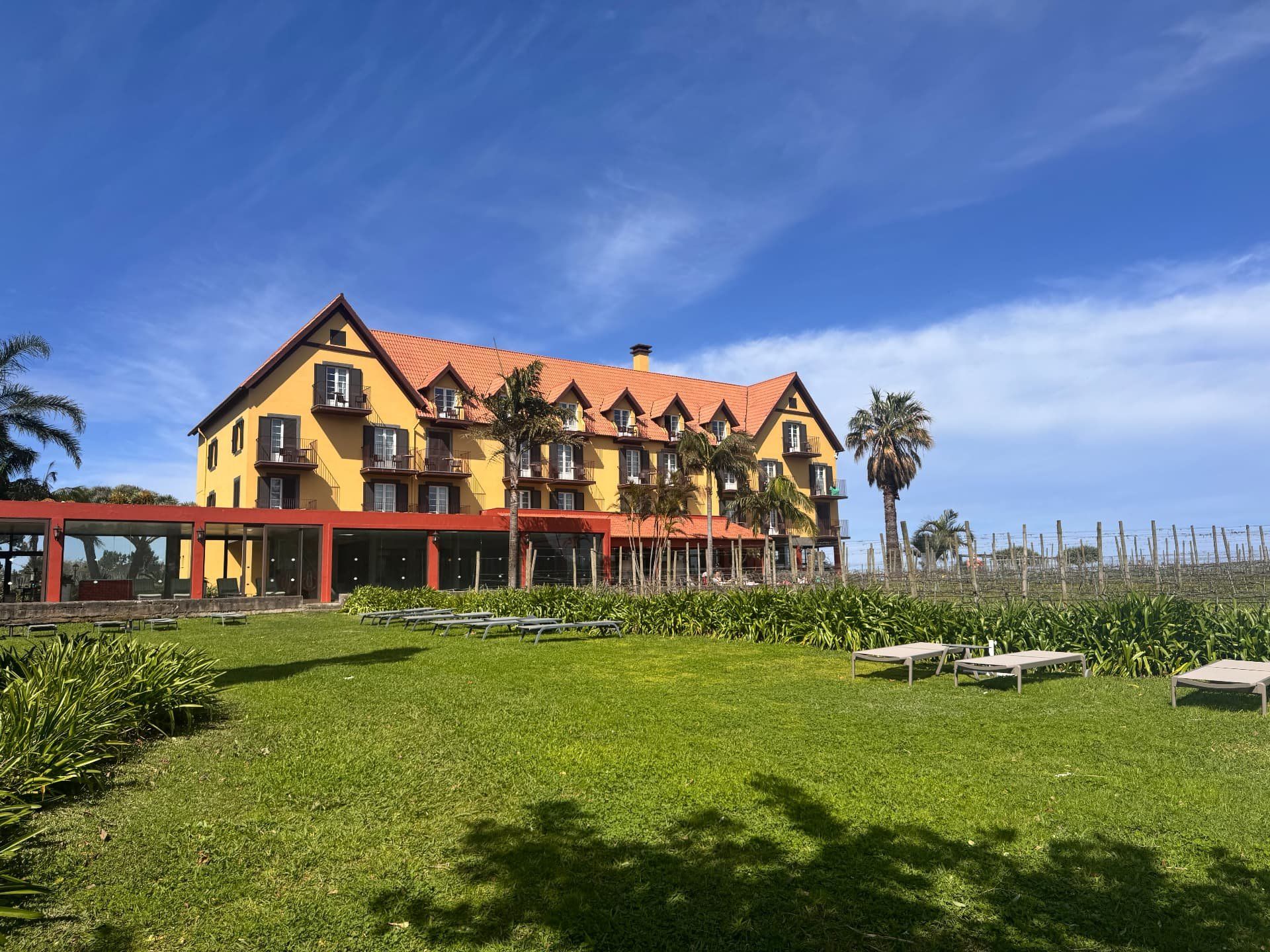 O hotel Quinta do Furao, em Santana, na Madeira, com fachada amarela, telhado vermelho, relvado e vinha