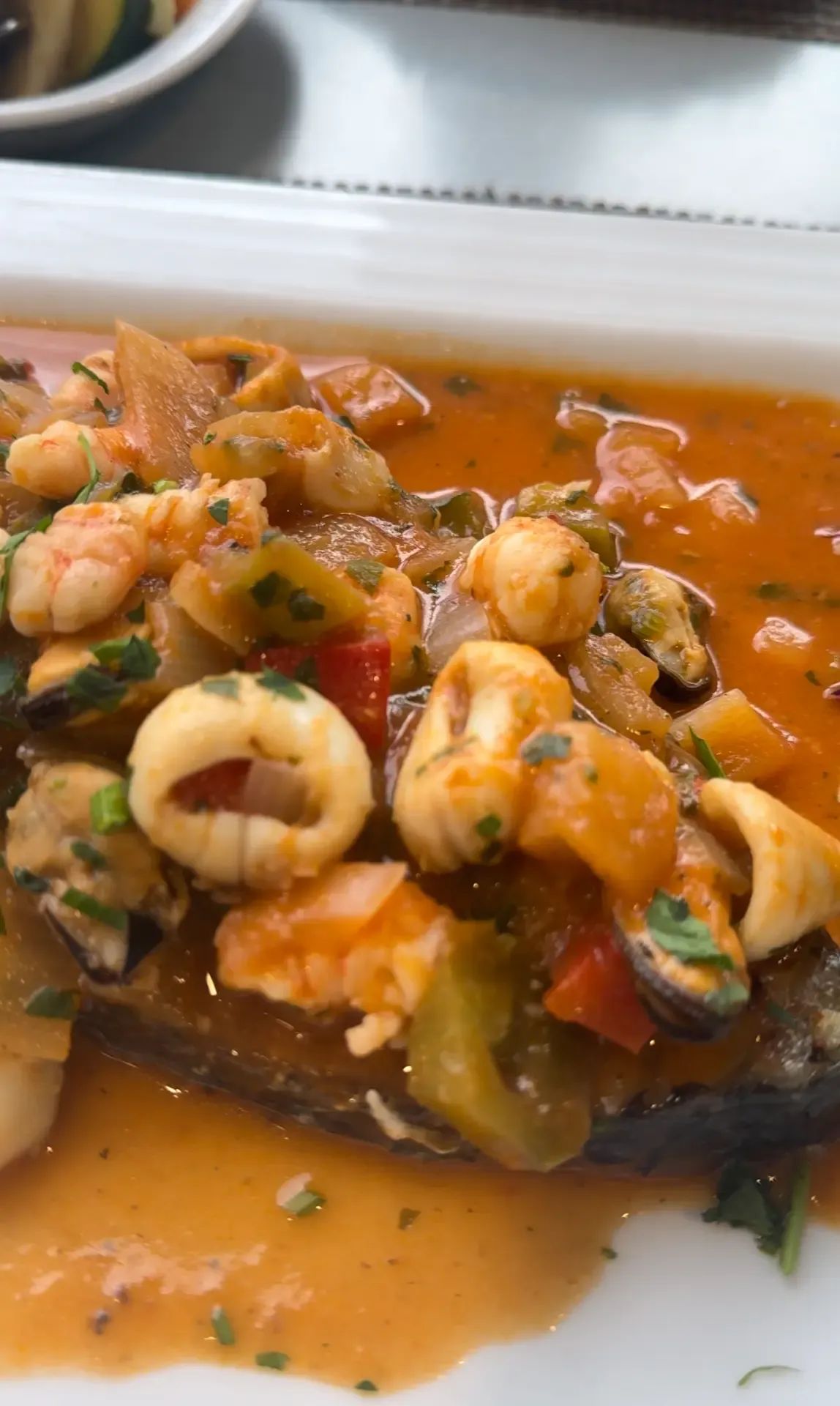Grilled fish topped with prawns, squid rings, mussels and peppers in a tomato sauce at A Traineira, Caniço