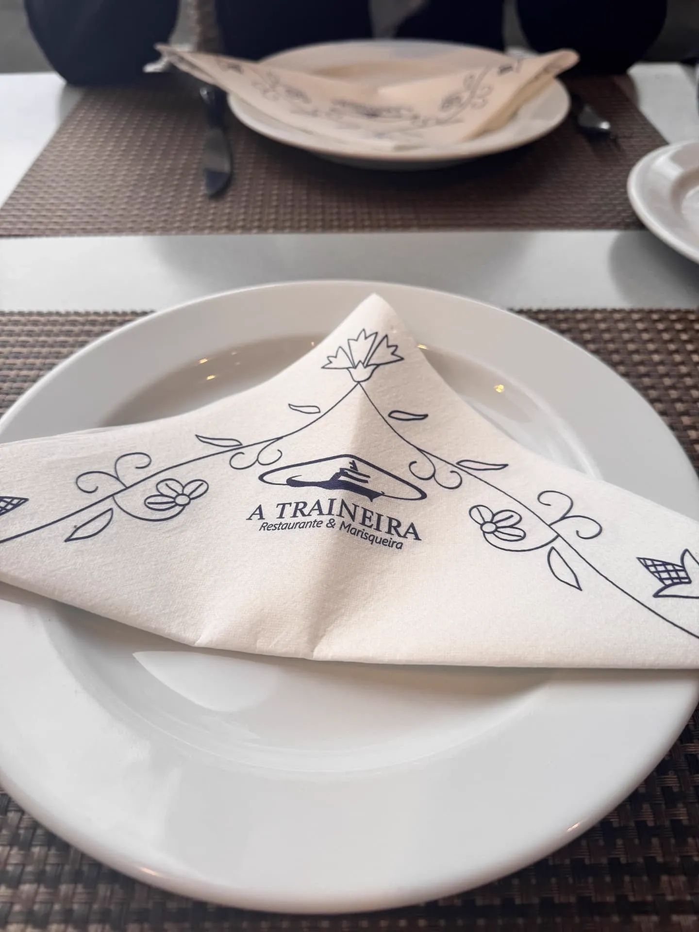 Table set with a folded A Traineira branded napkin on a white plate at the seafood restaurant in Caniço, Madeira