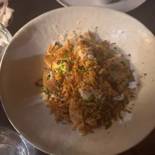 Food topped with chopped herbs and golden flakes in a wide ceramic bowl