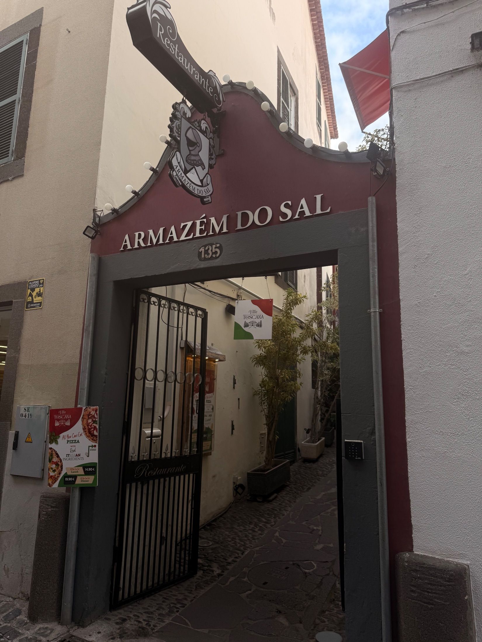 Entrada do Armazém do Sal com fachada vermelha, letreiro de restaurante e portão de ferro aberto