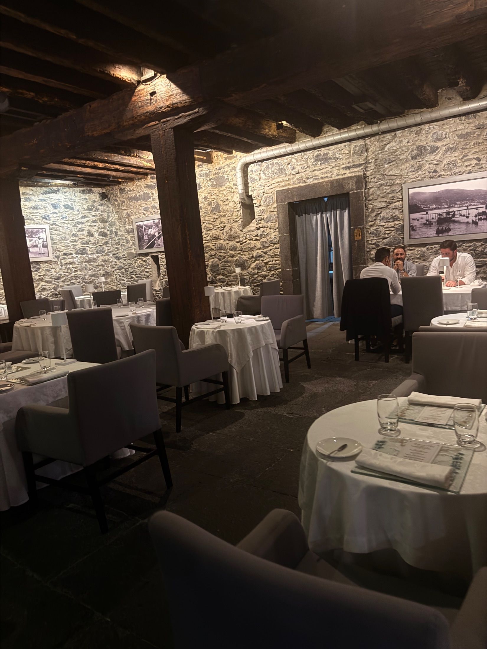 Restaurant dining room with stone walls, exposed wooden beams and white tablecloths