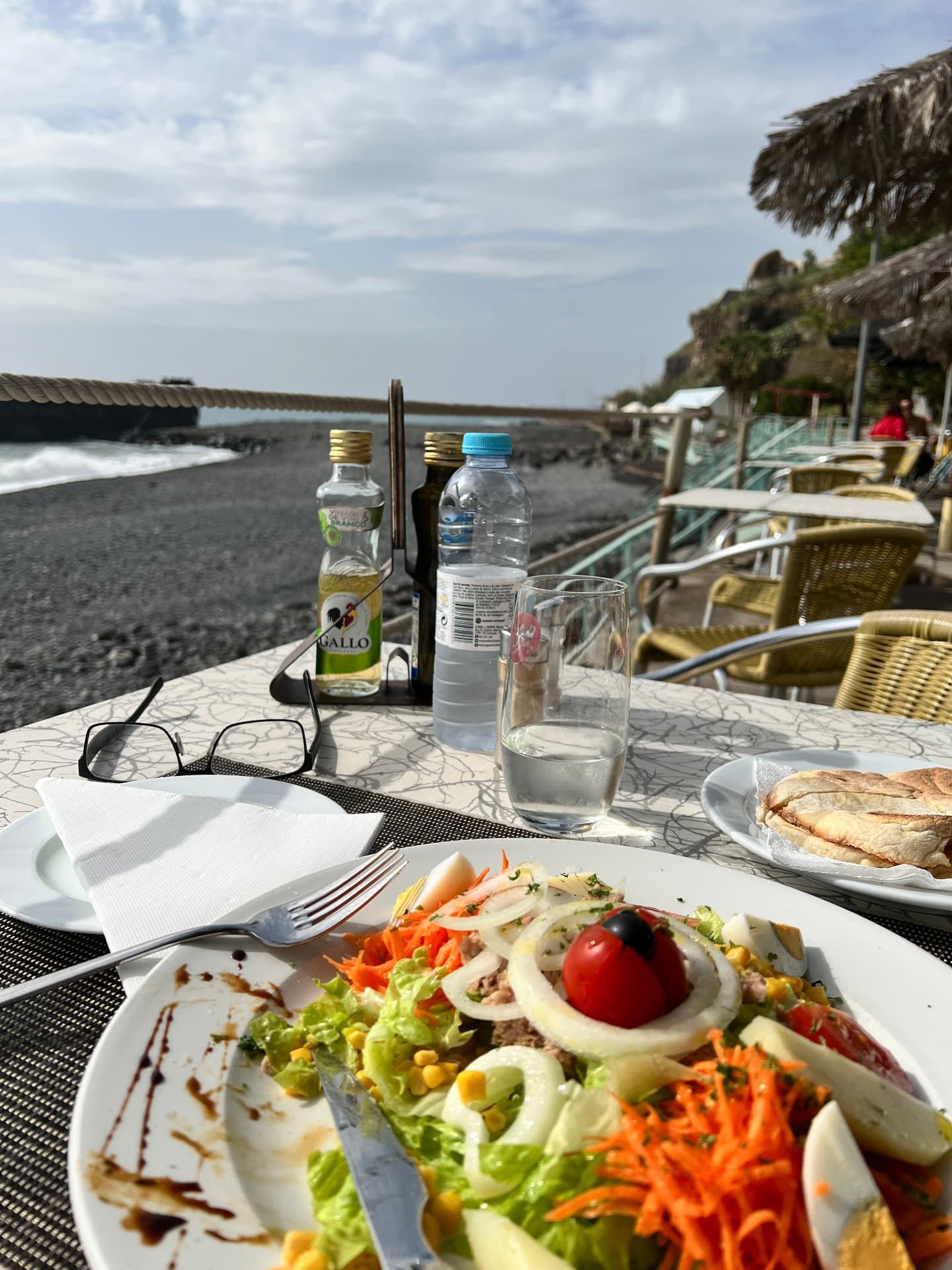 Mixed salad and bolo do caco sandwich on the seafront terrace at Beira Calhau in Funchal, Madeira, with the pebble beach and Atlantic behind