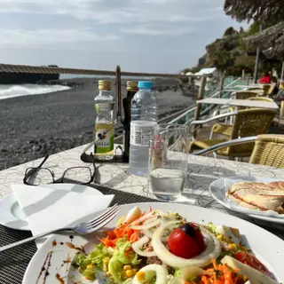 Mixed salad and bolo do caco sandwich on the seafront terrace at Beira Calhau in Funchal, Madeira, with the pebble beach and Atlantic behind