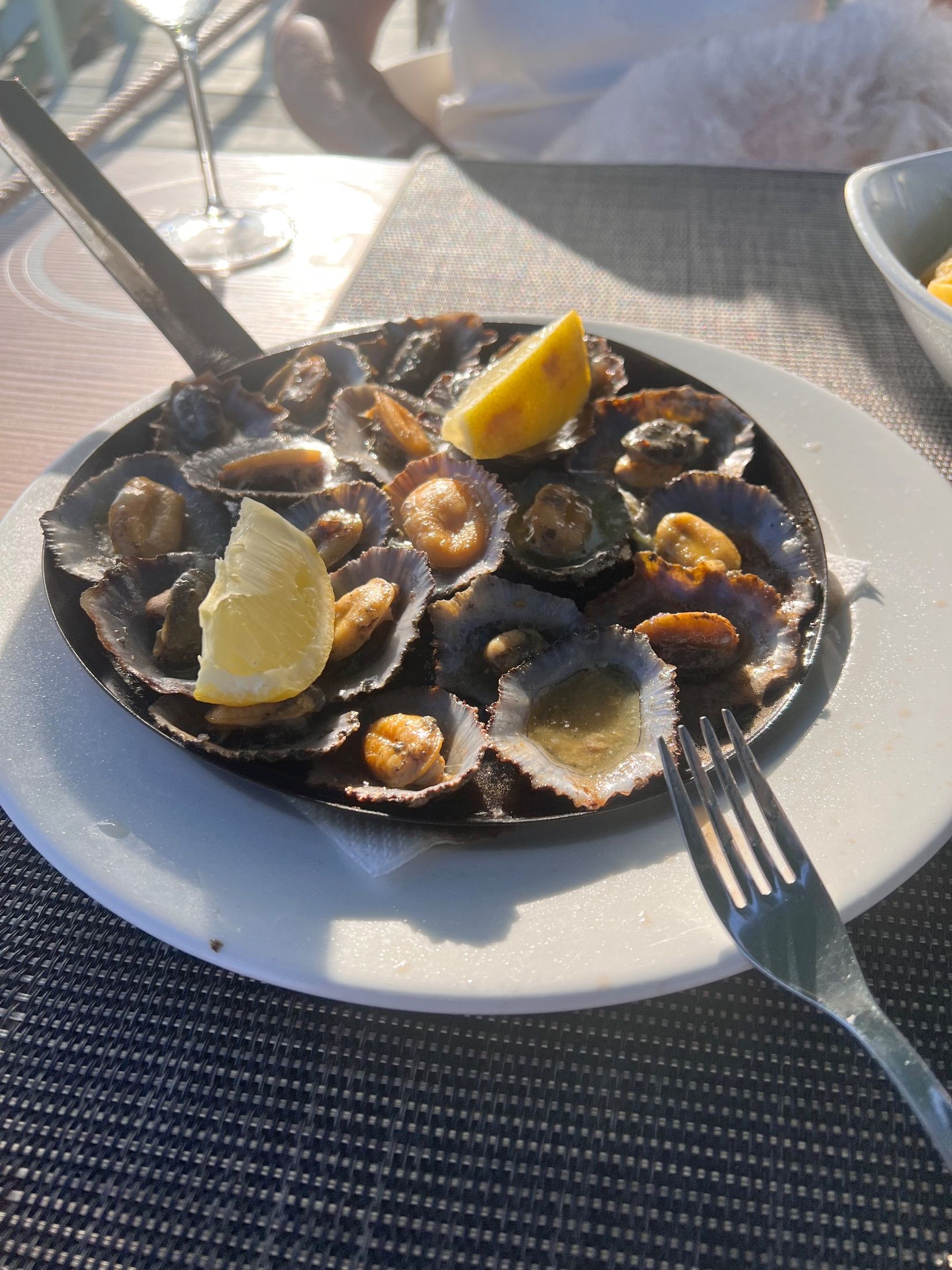 Limpets in their shells with lemon wedges on a black serving pan