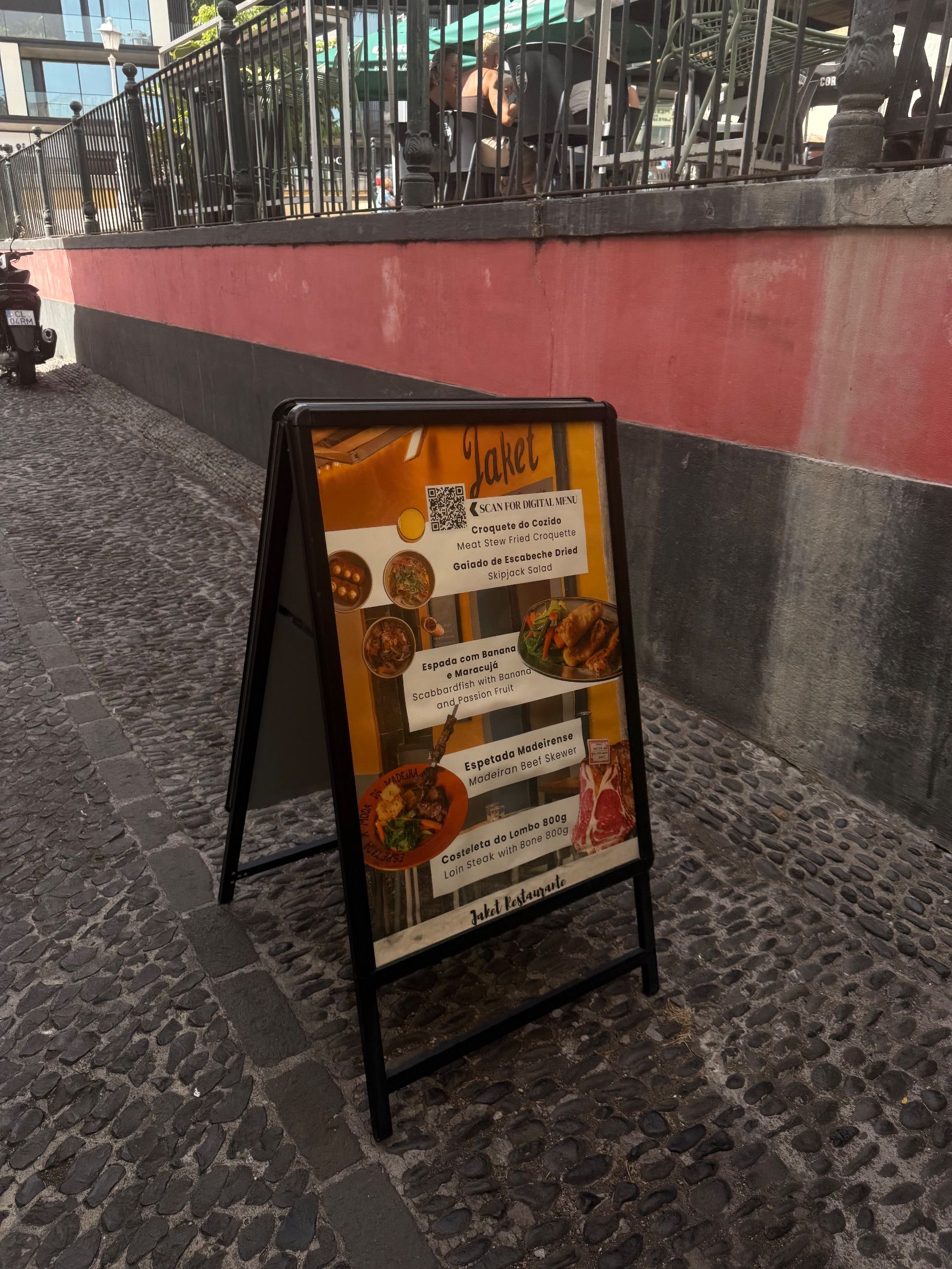 Painel de ementa no passeio de calçada, abaixo de uma esplanada elevada