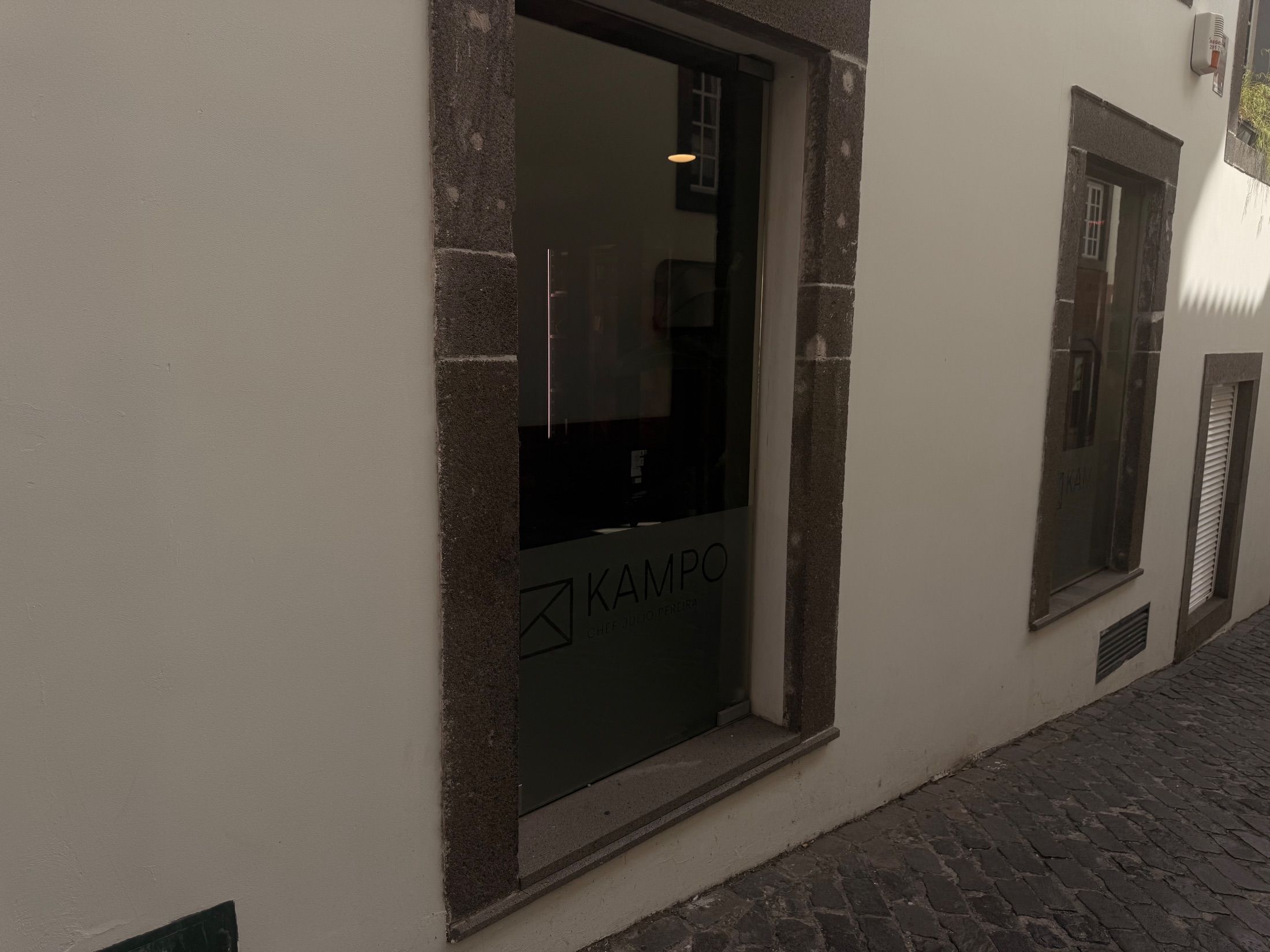 Nome Kampo no vidro sob cantarias escuras na fachada branca do restaurante