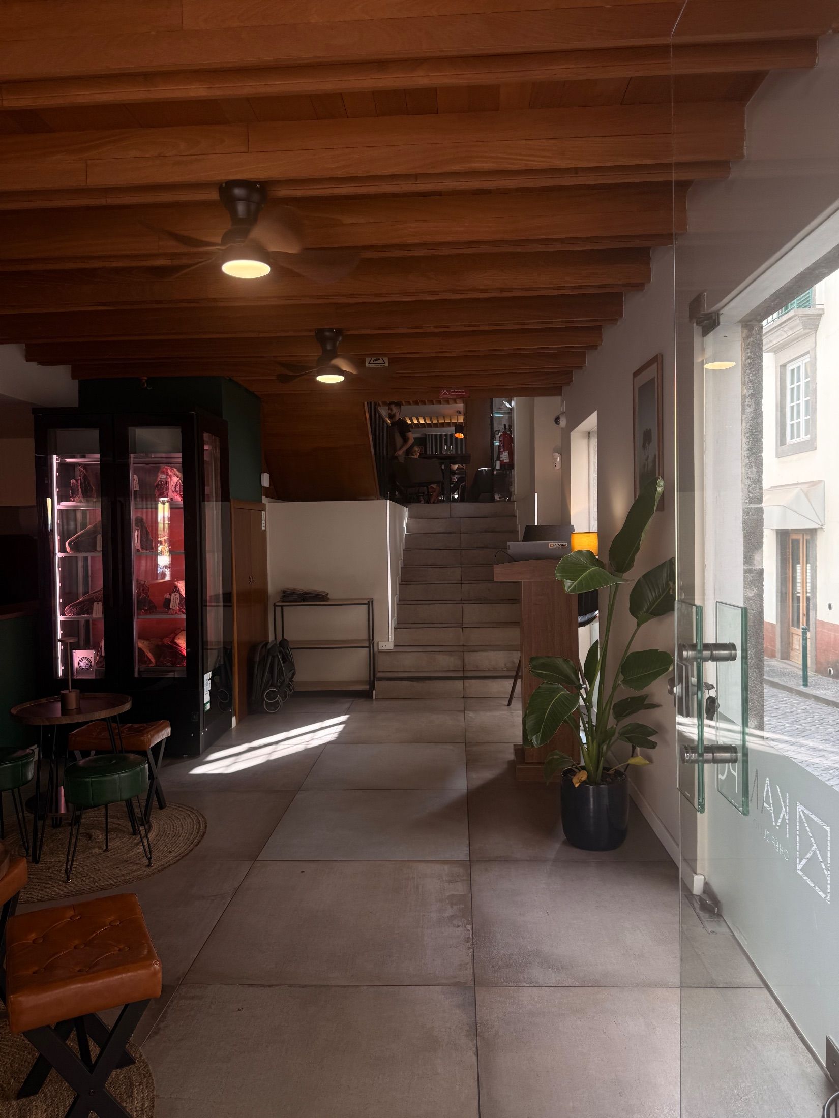 Restaurant entrance with meat display cabinet, wooden ceiling and stairs to a dining area