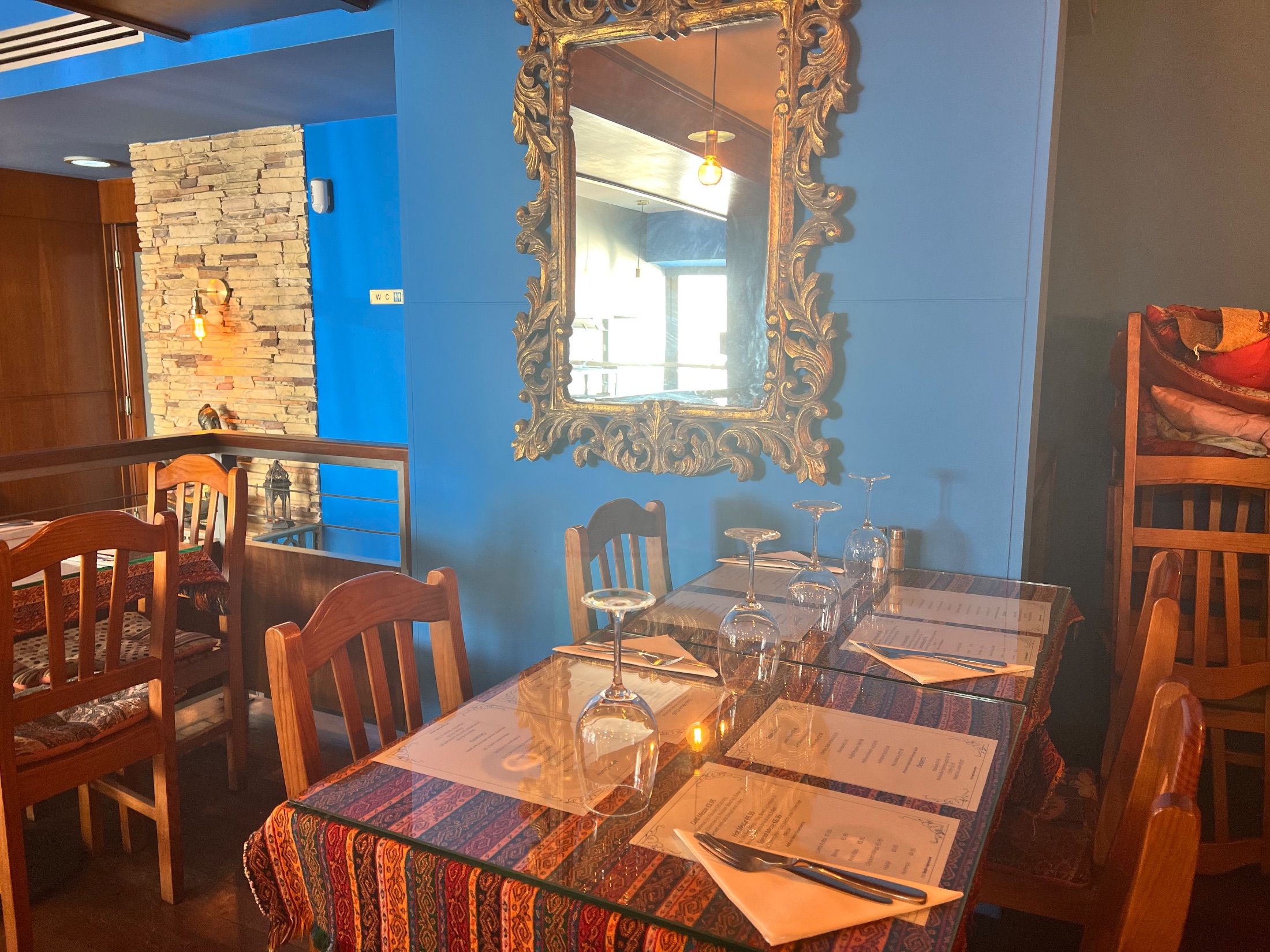 Restaurant tables with wooden chairs, blue walls and an ornate gold-coloured mirror