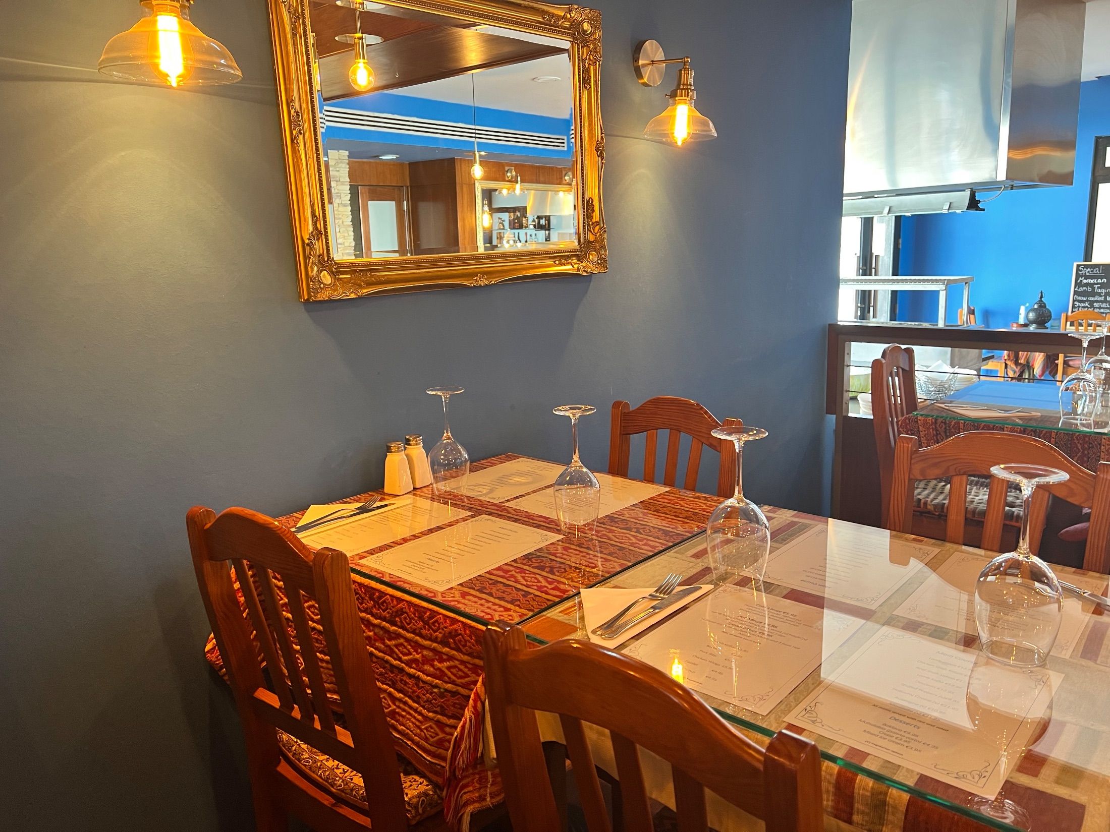 Restaurant tables with wooden chairs, inverted wine glasses and a gold-framed wall mirror