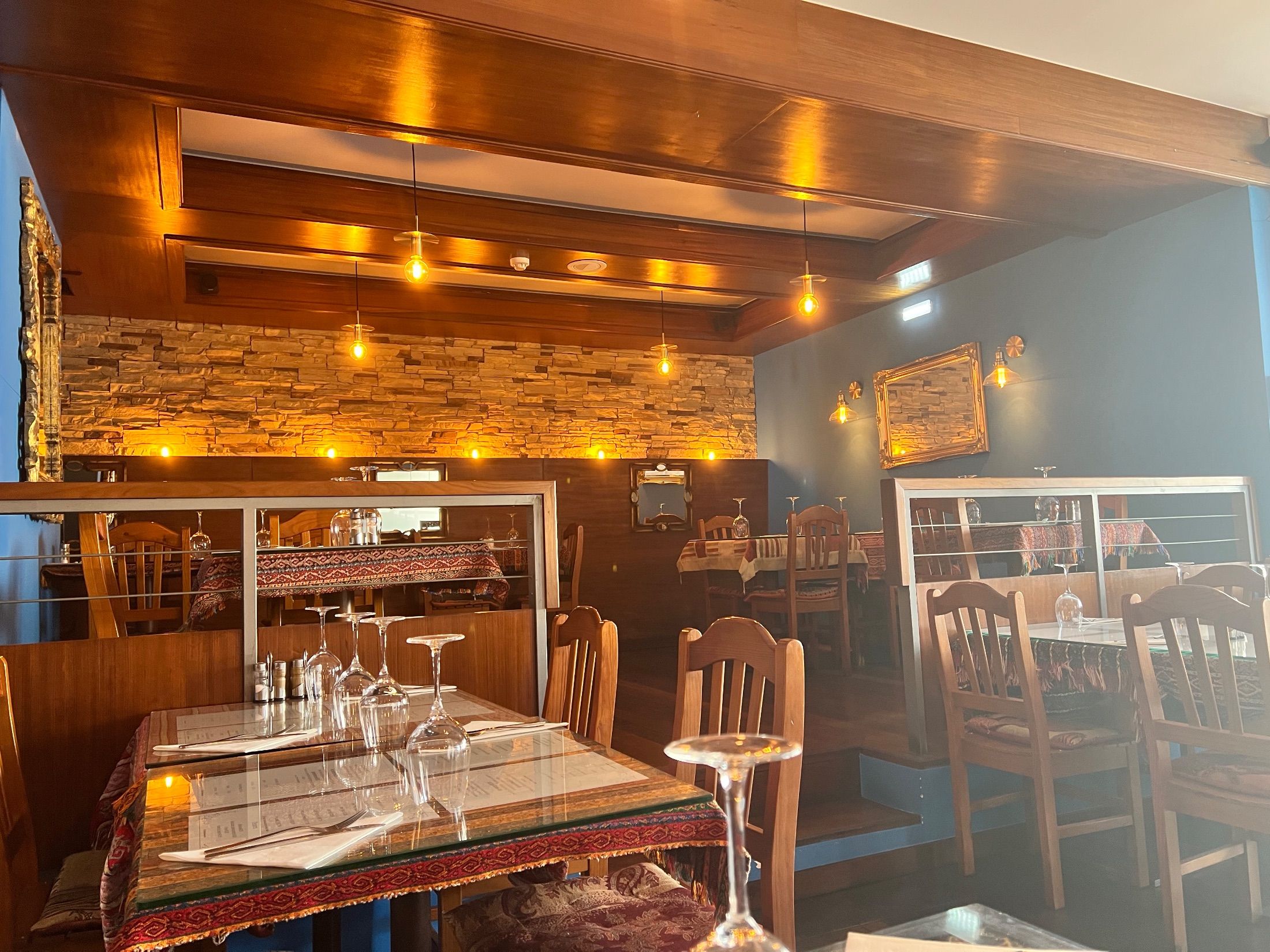 Restaurant interior with wooden chairs, patterned tablecloths, stone wall cladding and pendant lights