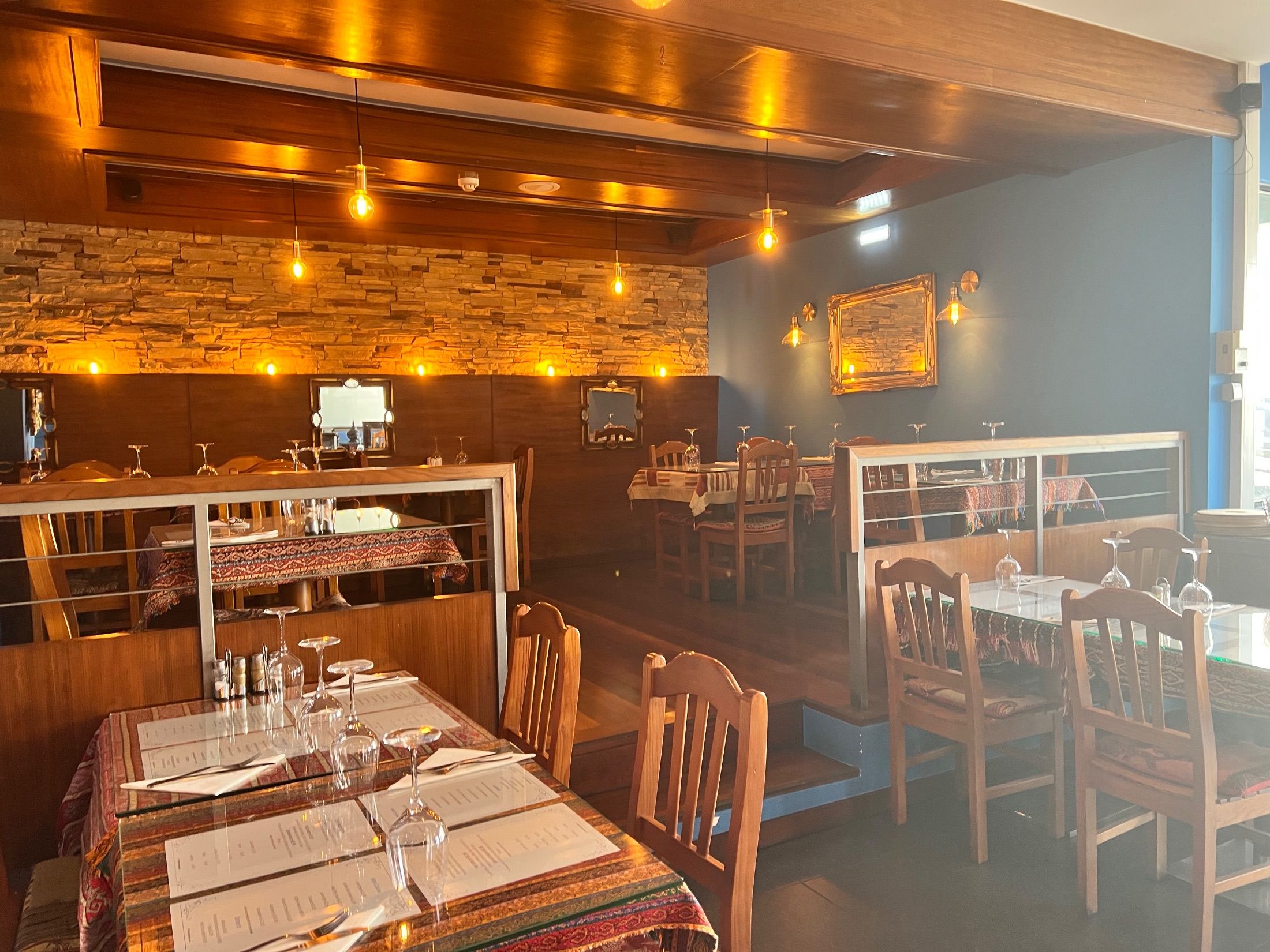 Restaurant interior with wooden chairs, patterned tablecloths, stone wall cladding and pendant lights