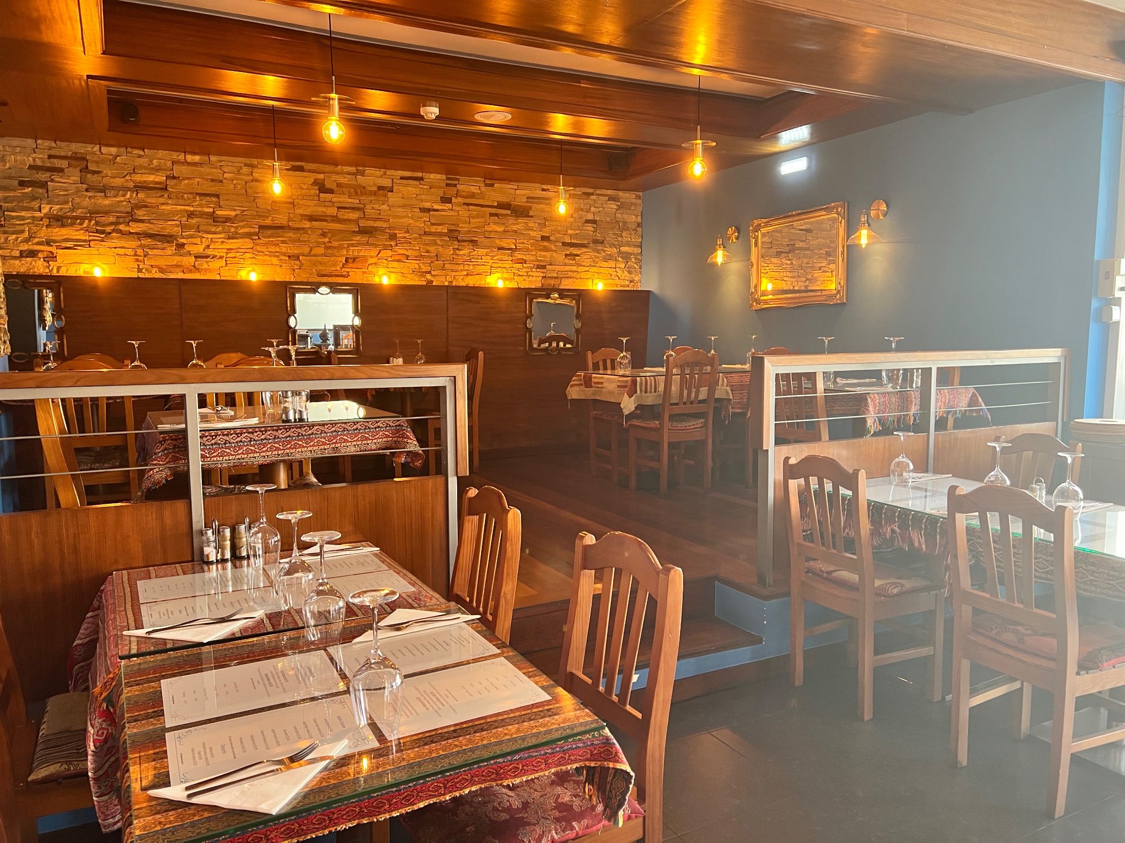 Restaurant interior with wooden chairs, patterned tablecloths, stone walls and hanging lights