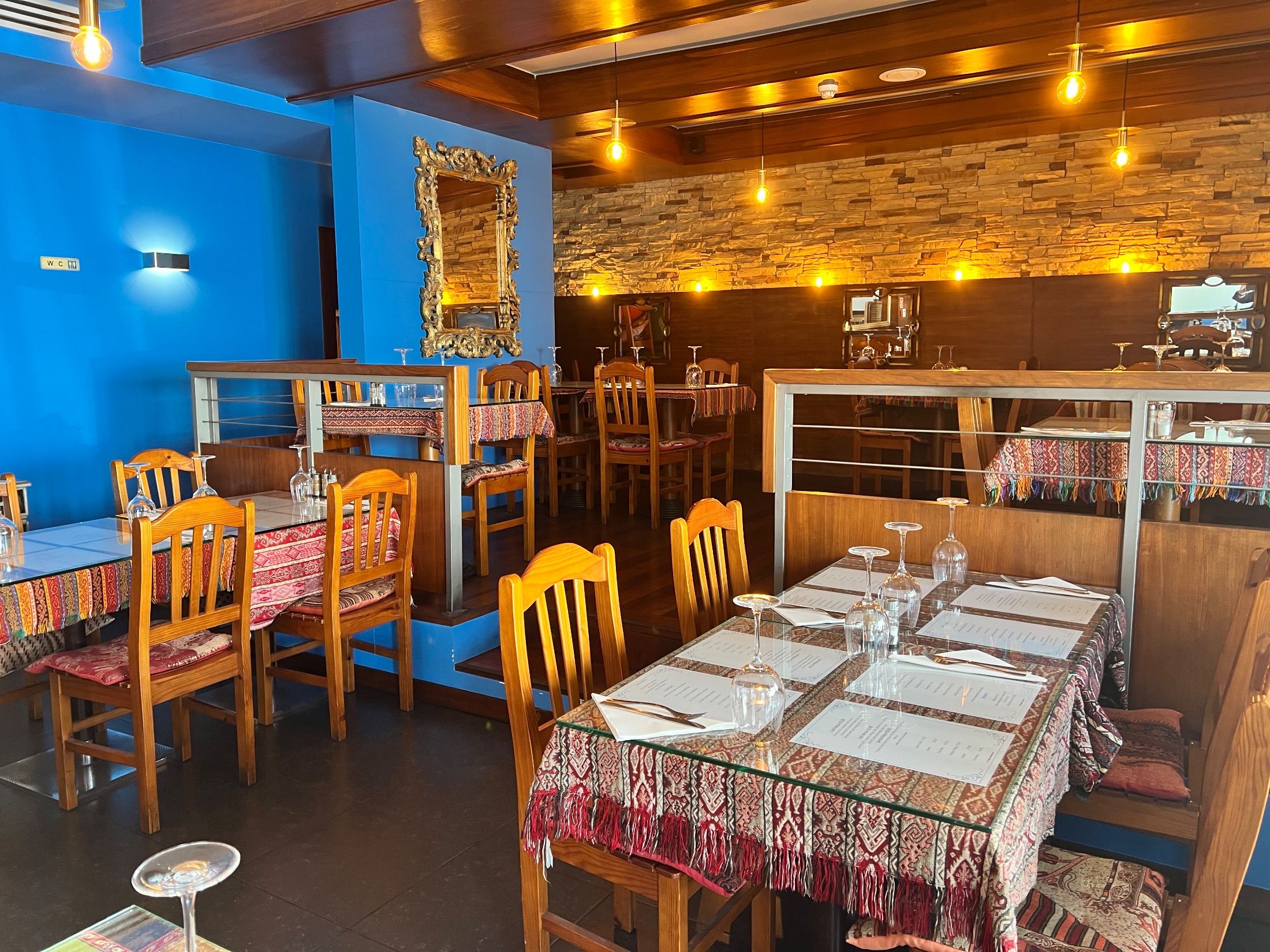 Restaurant interior with blue walls, wooden chairs, patterned tablecloths and hanging light bulbs