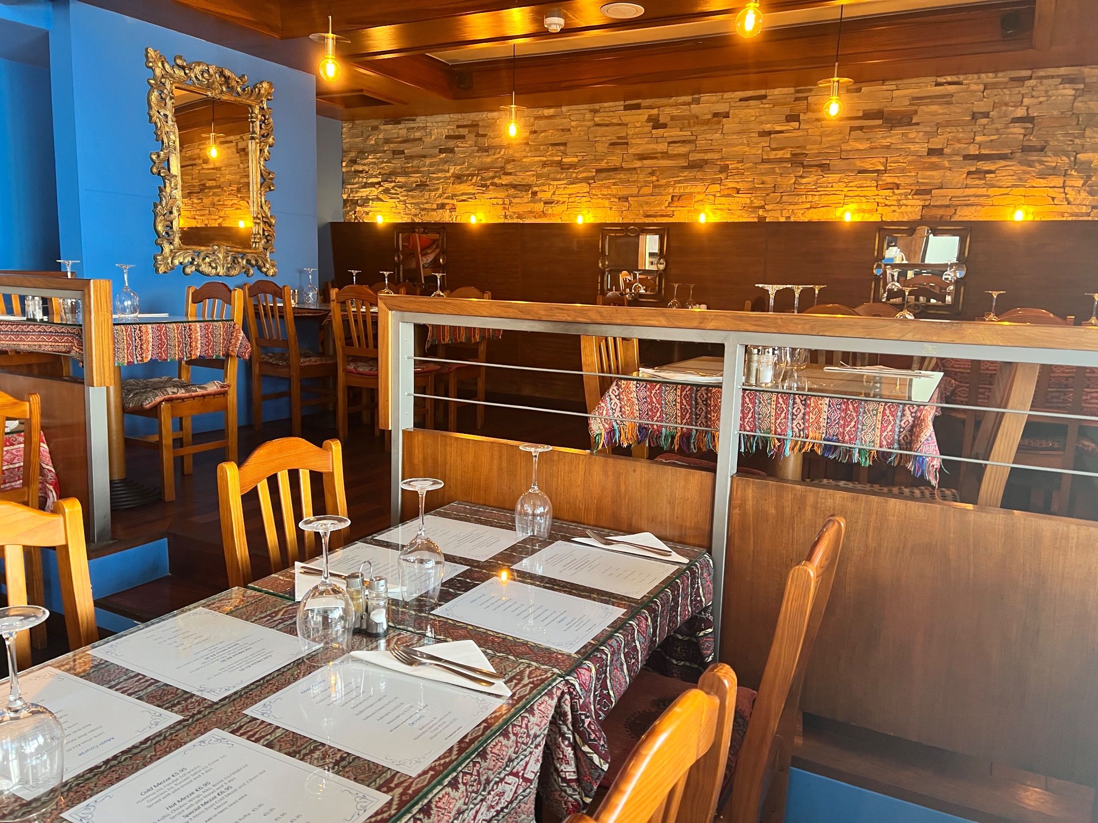 Restaurant interior with patterned tablecloths, wooden chairs, ornate mirrors and hanging bulbs