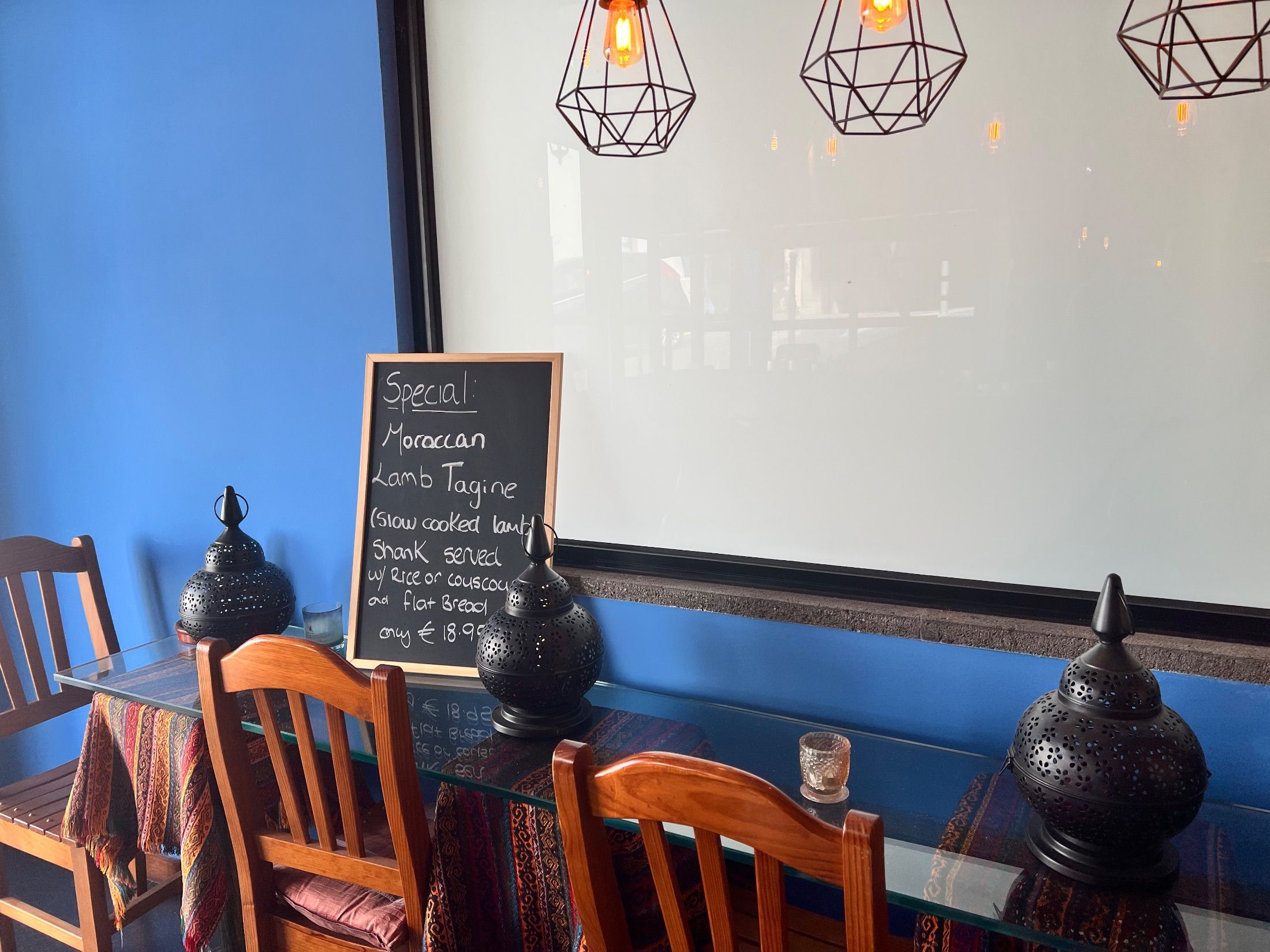 Restaurant seating with wooden chairs, black metal lanterns and a chalkboard against blue walls