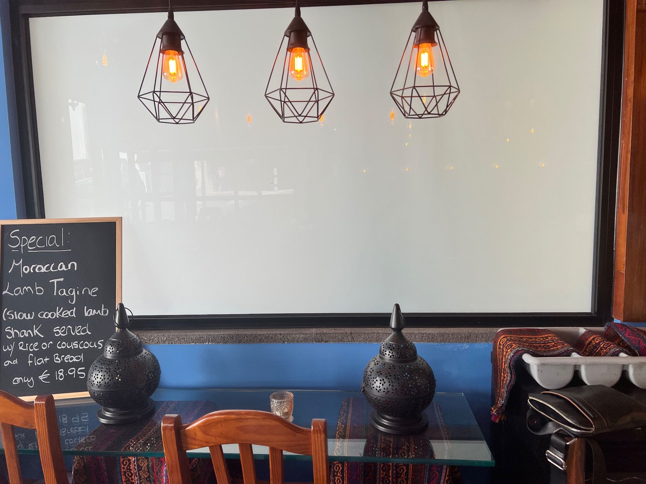 Restaurant table with pierced metal lanterns, wooden chairs and three geometric pendant lights