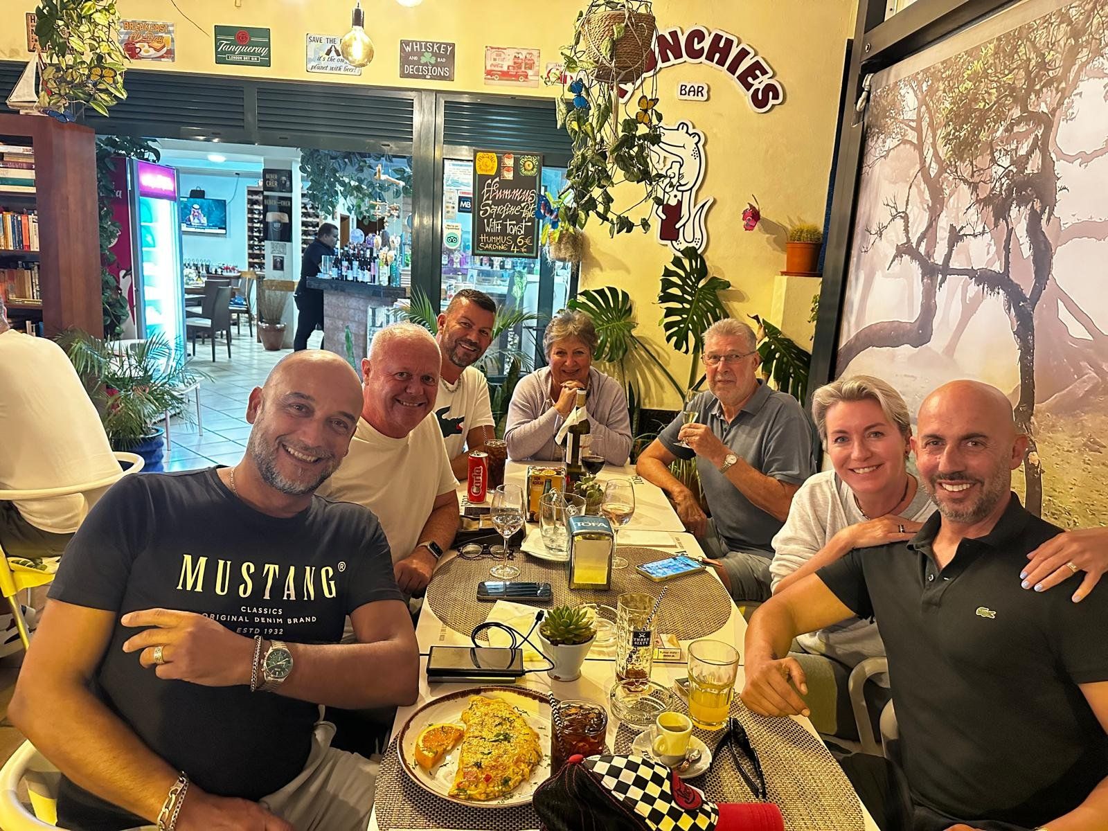 Friends enjoying dinner and drinks at Munchies Restaurante & Bar in Caniço, Madeira, with the bar's quirky decor and omelette dish on the table