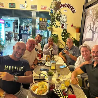 Friends enjoying dinner and drinks at Munchies Restaurante & Bar in Caniço, Madeira, with the bar's quirky decor and omelette dish on the table