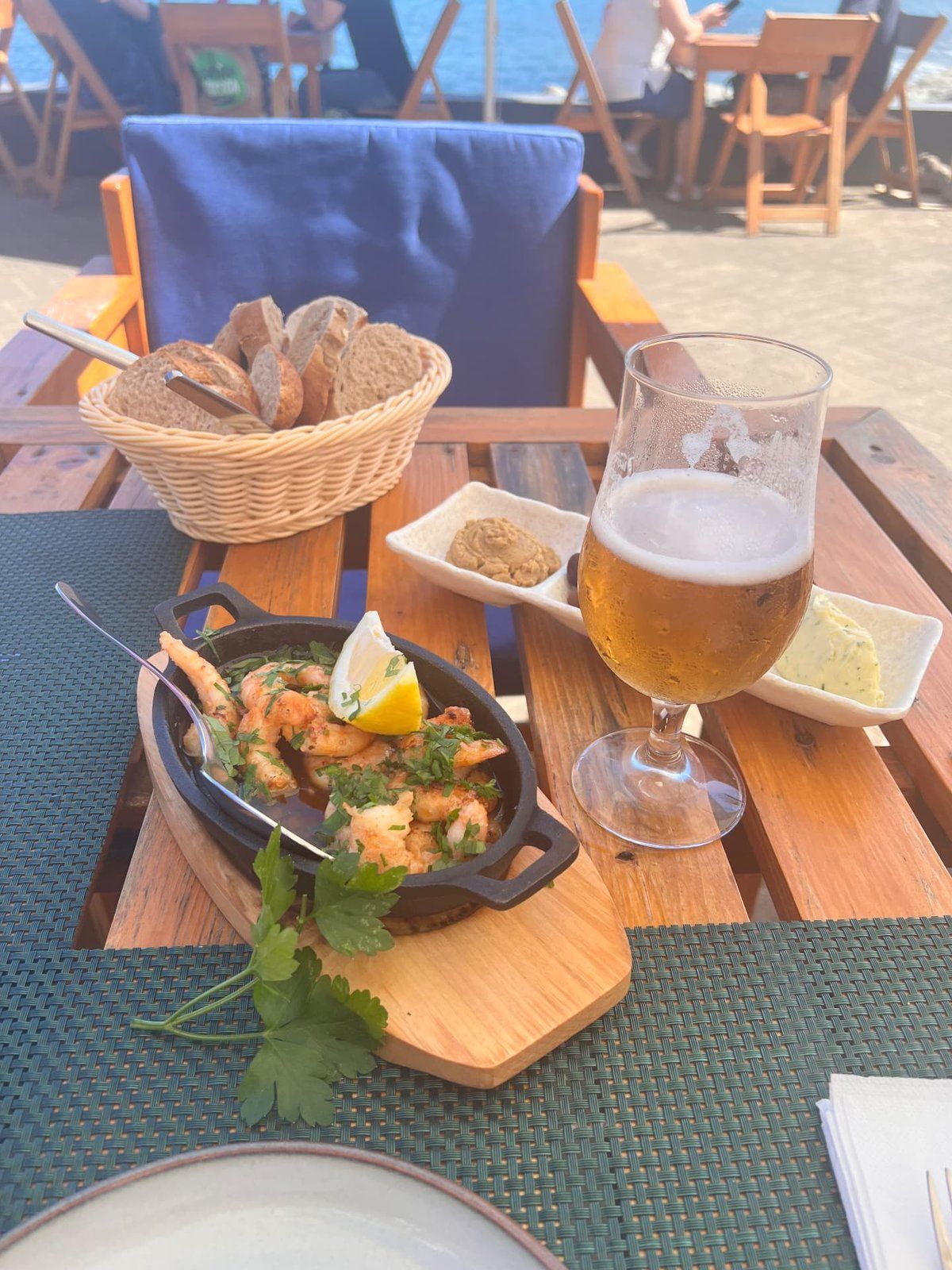 Garlic prawns in a cast iron pan with a cold beer and bread basket at Praca do Engenho restaurant terrace overlooking the sea in Porto da Cruz, Madeira