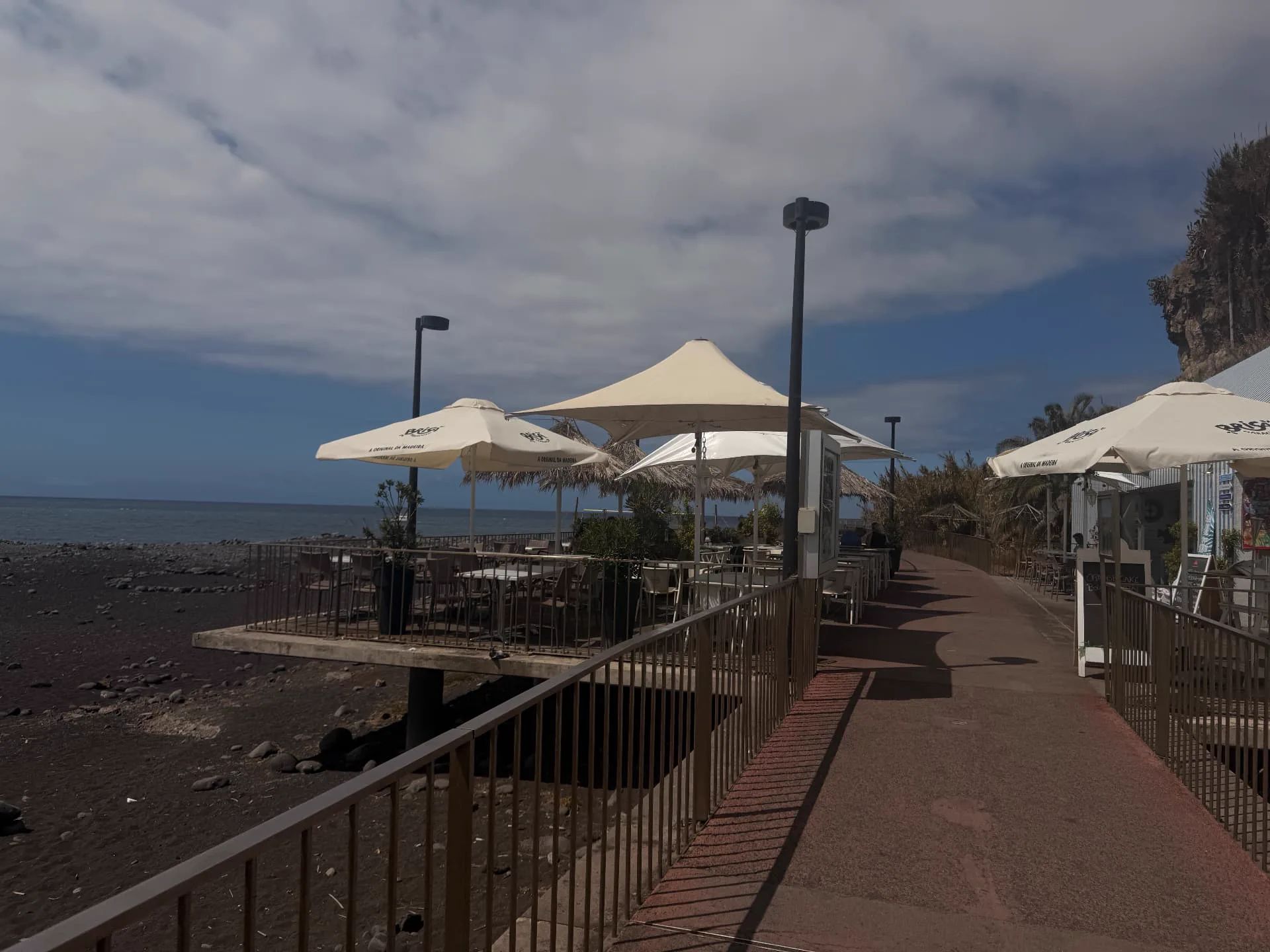 Seafront esplanade of Restaurante Praia Formosa with parasols right on the black pebble beach, Funchal