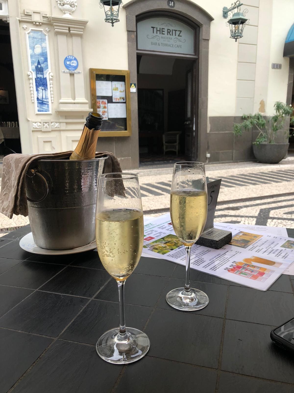 Two glasses of sparkling wine on a terrace table at The Ritz Cafe, Funchal, with the bar and terrace cafe entrance behind